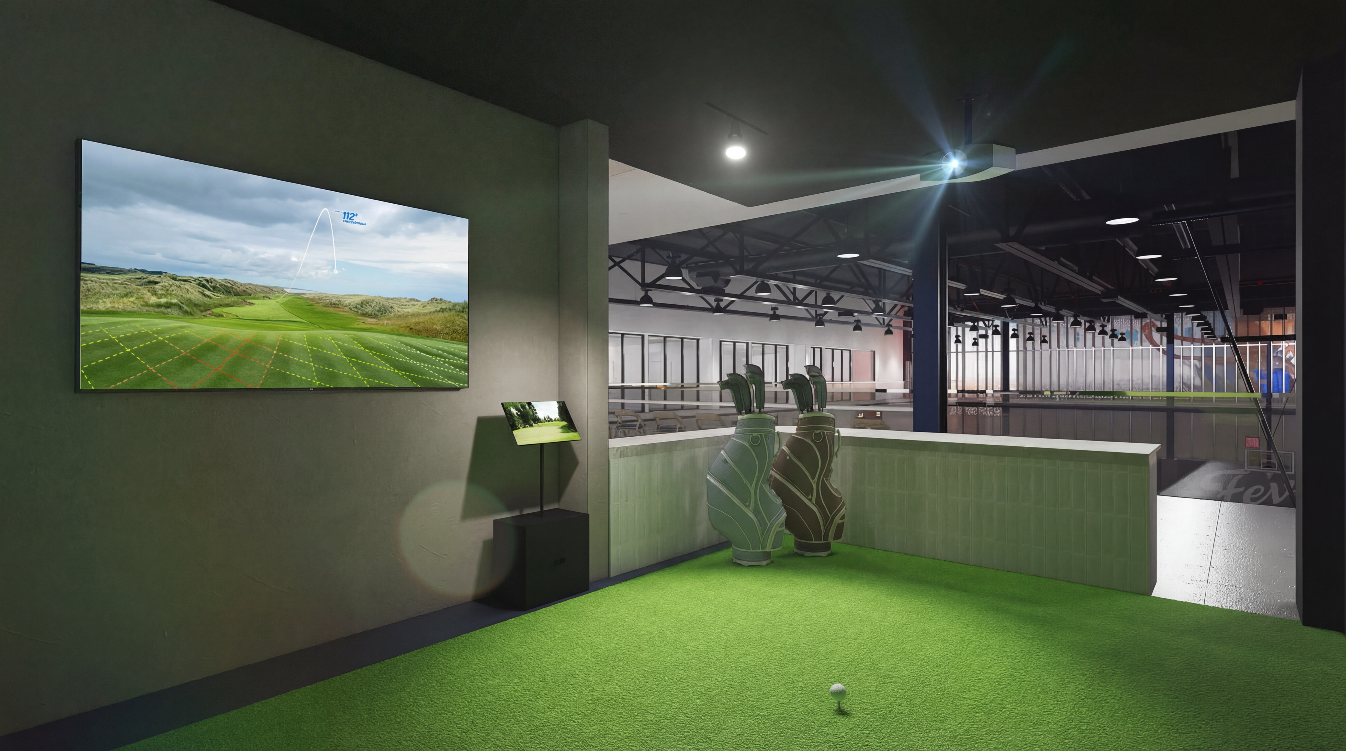 Indoor golf simulator: a large wall screen shows a green course with grid lines; two green golf bags stand by a low wall; a pedestal display; a tee with a ball on bright green turf.