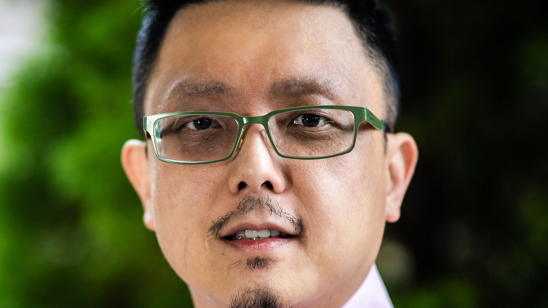 A man stands for a portrait in front of a green background. 