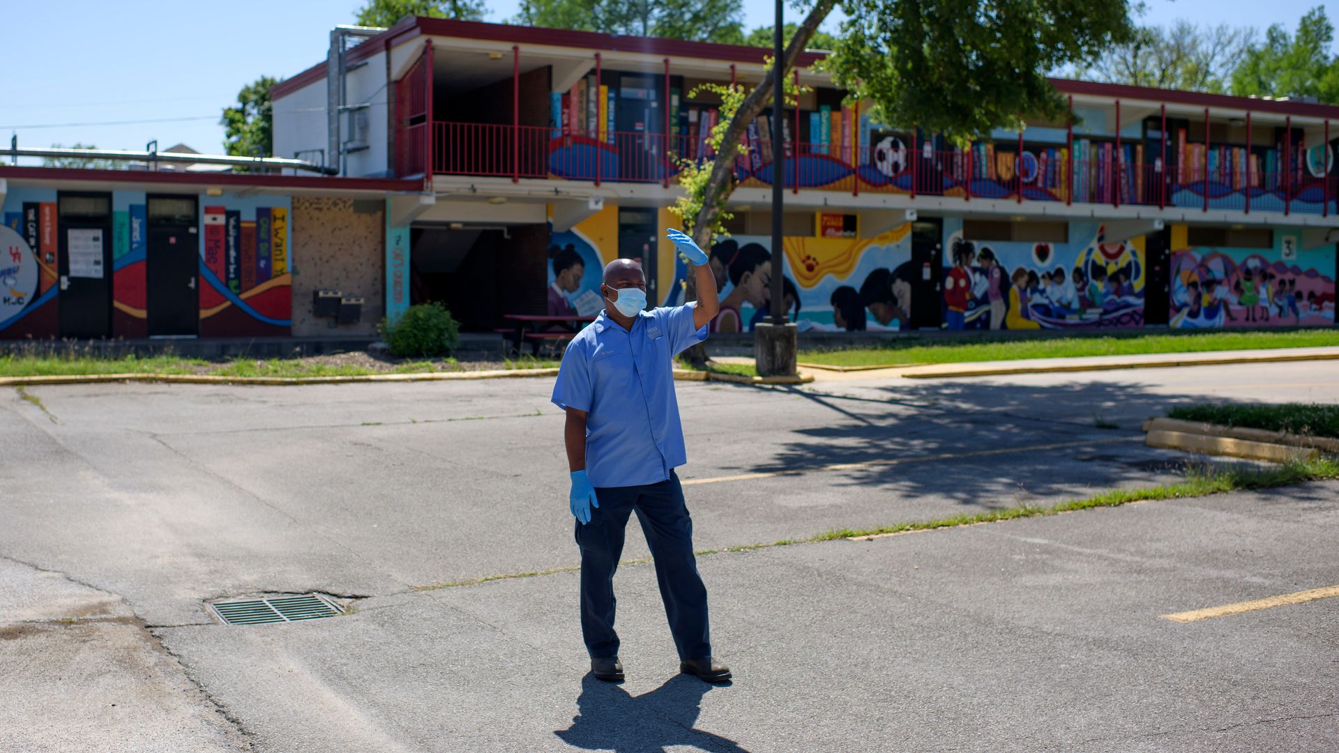 A volunteer wearing a mask and gloves stands outside of a school to gather donations