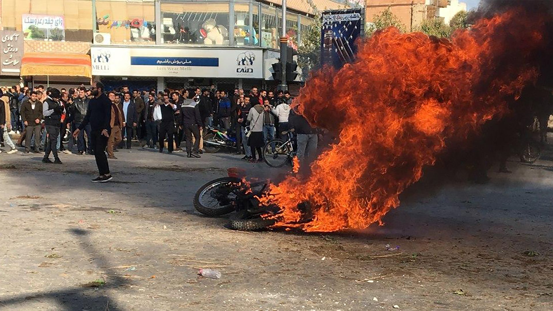 protestors surround a burning motorcycle in a street intersection
