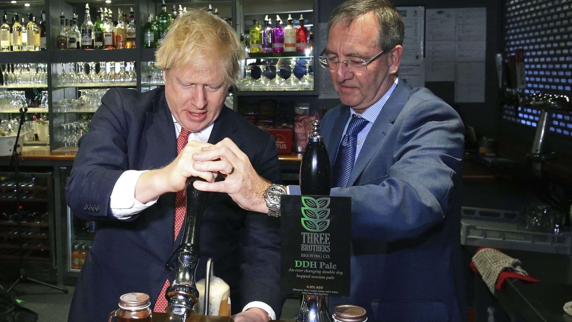 In this image, Boris Johnson stands behind the counter in a bar and pulls down a pint