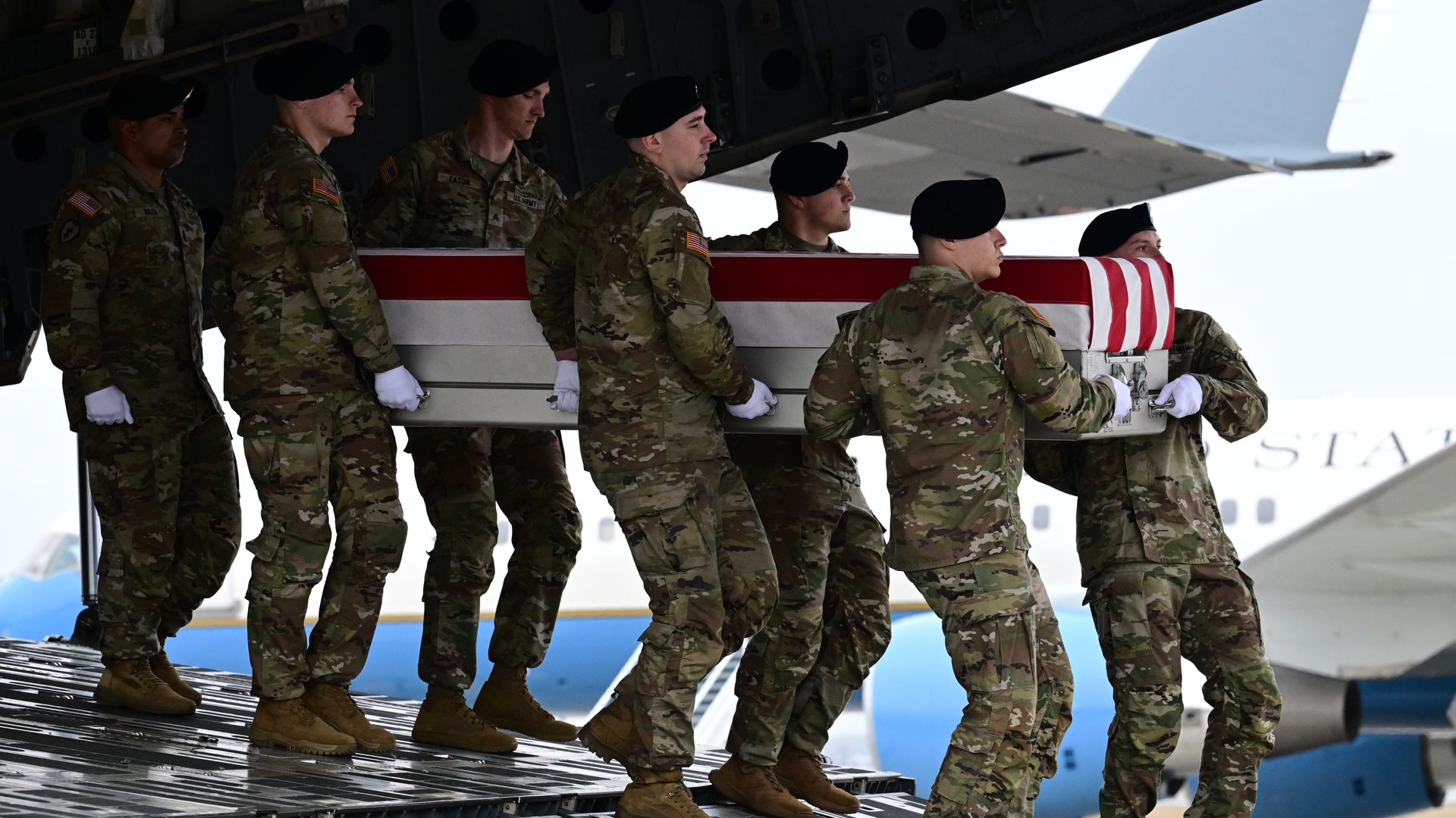 A group of soldiers removing a coffin from a plane draped with an American flag