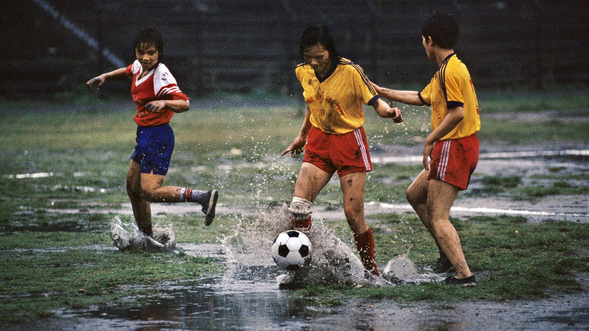 Three women playing soccer in the rain