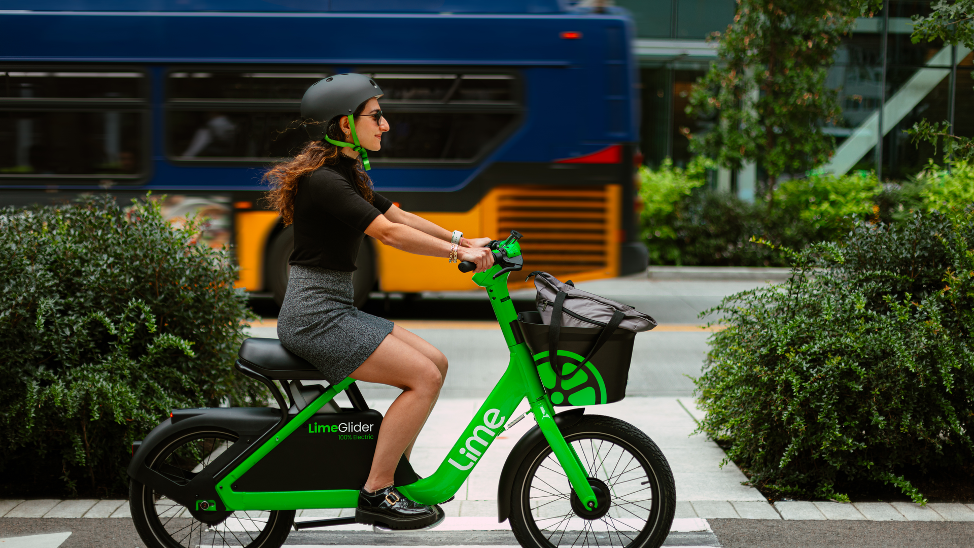 A person rides a green bike-like scooter on a street as a Metro bus passes in the background.