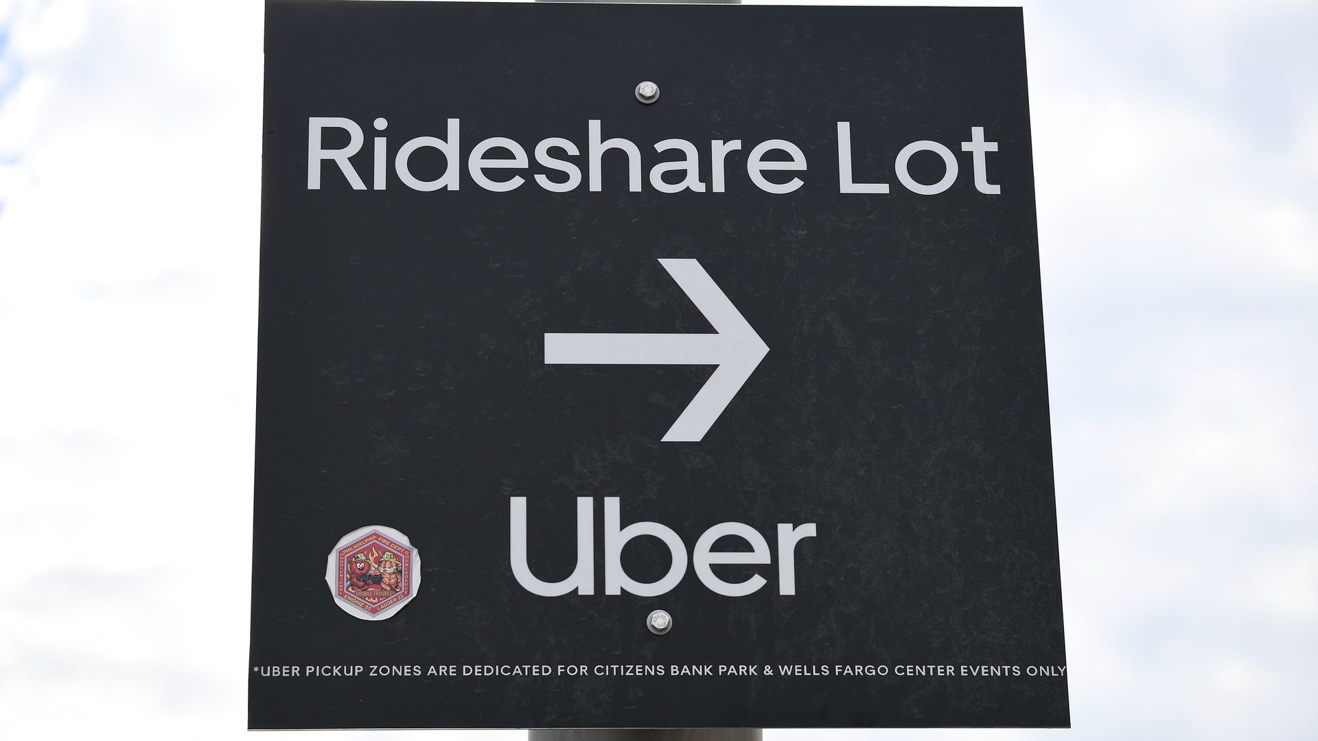 A close up view of a sign for a Rideshare Lot with the Uber logo outside Citizens Bank Park.
