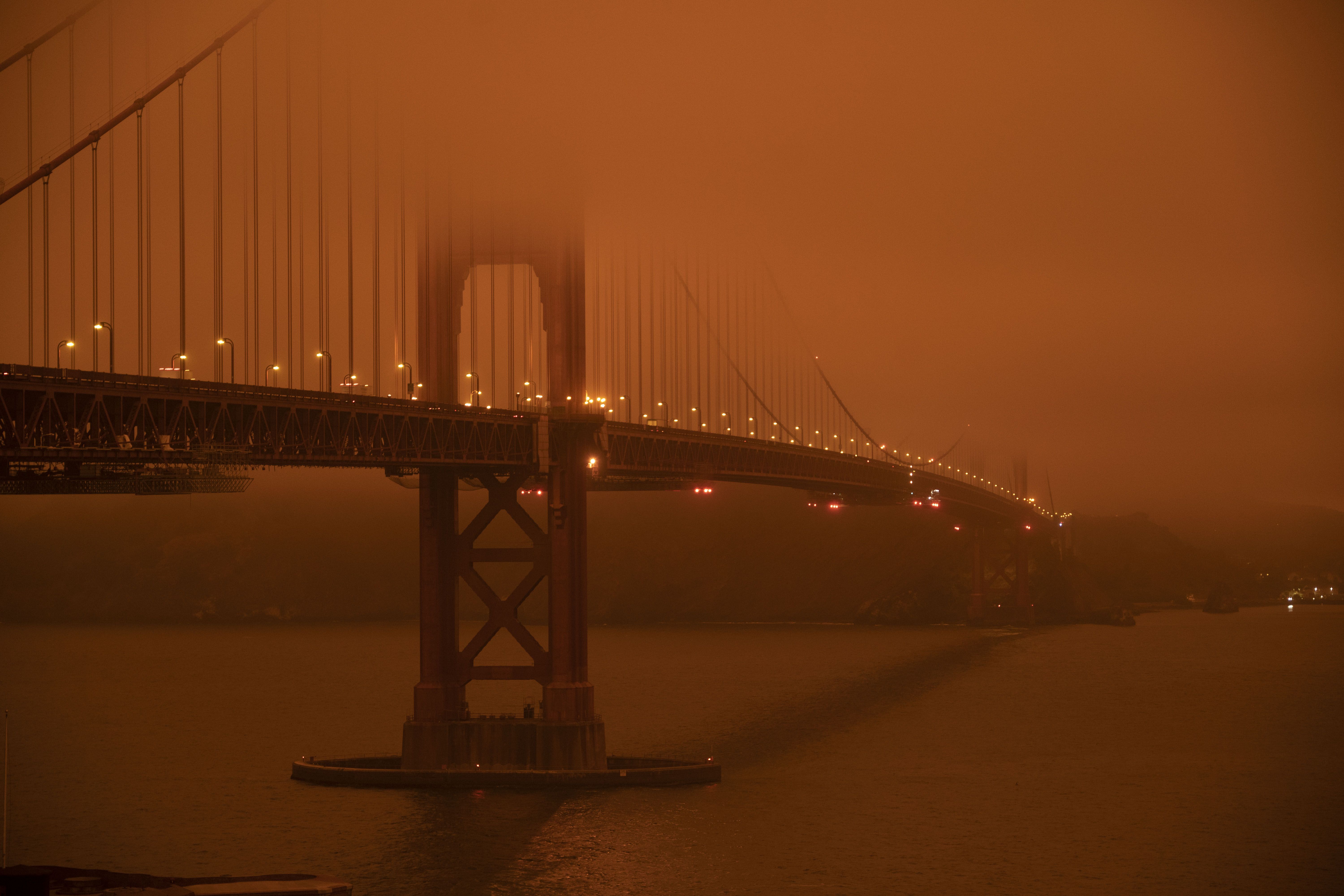 Cars drive along the Golden Gate Bridge under an orange smoke filled sky at midday in San Francisco