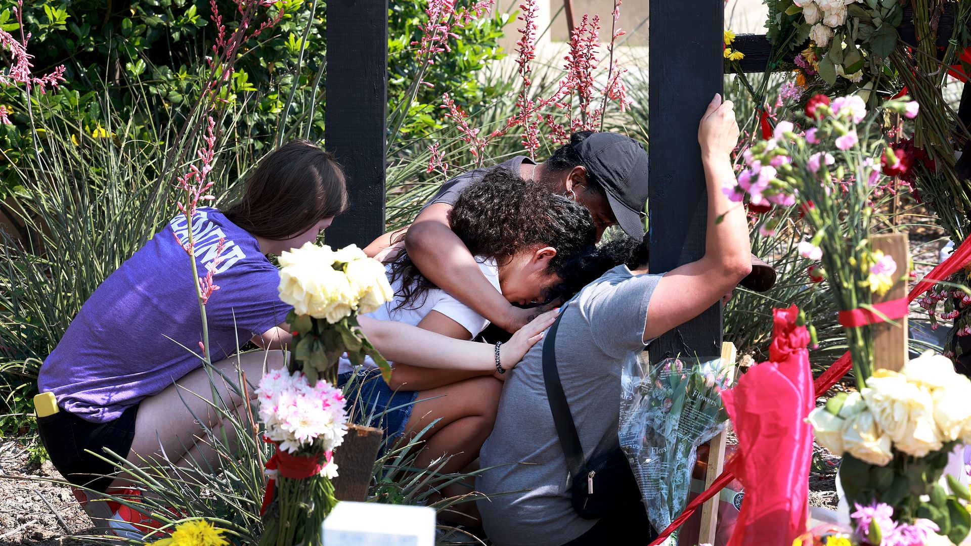 A mother is comforted as she visits a cross that bears the name of one of her children's best friends at the memorial set up near the scene of a mass shooting at the Allen Premium Outlets mall on May 9, 2023 in Allen, Texas.