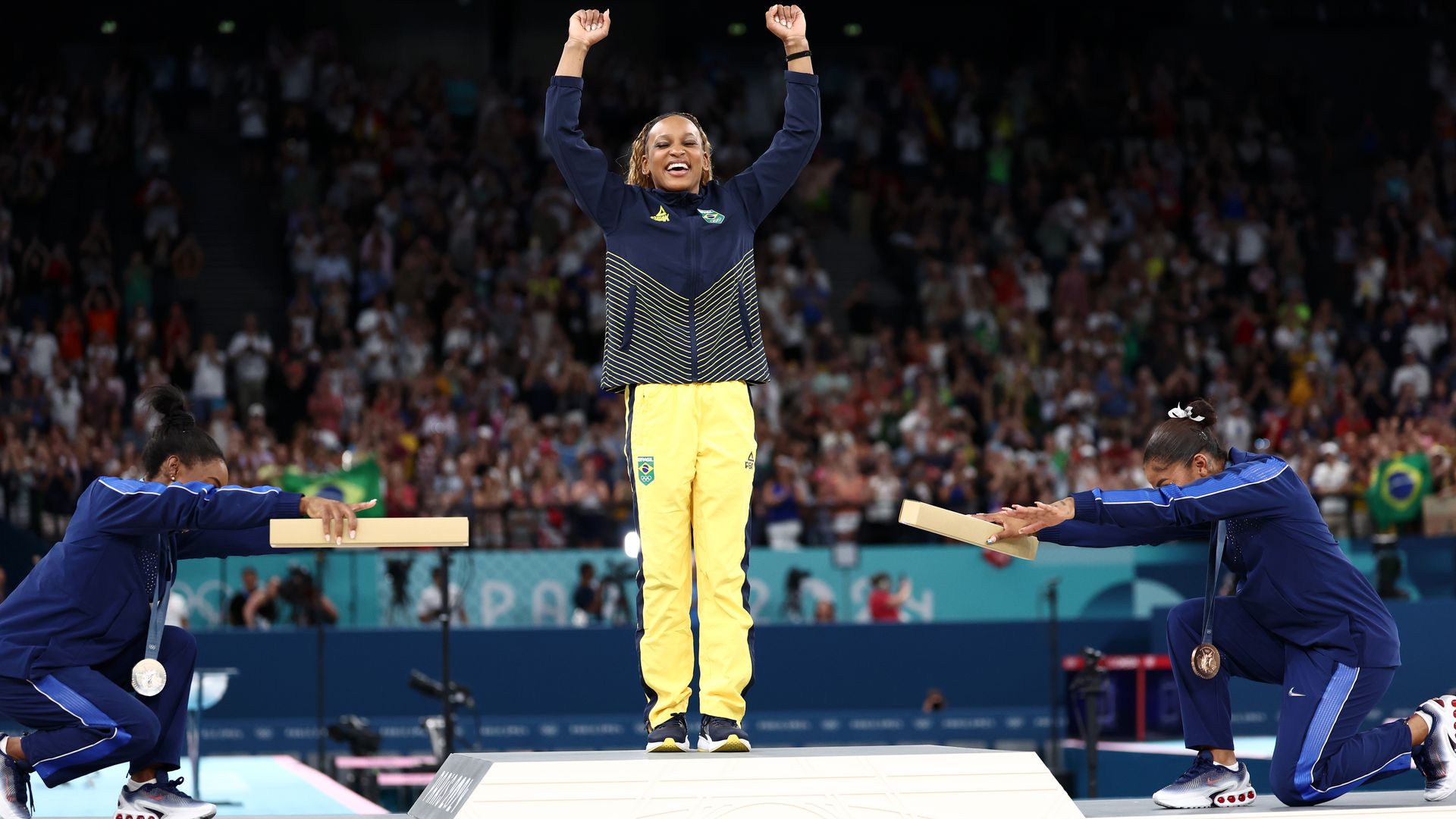 American gymnasts Jordan Chiles and Simone Biles bow in appreciation to gold medalist Rebeca Andrade of Brazil during the medal ceremony for floor exercise.