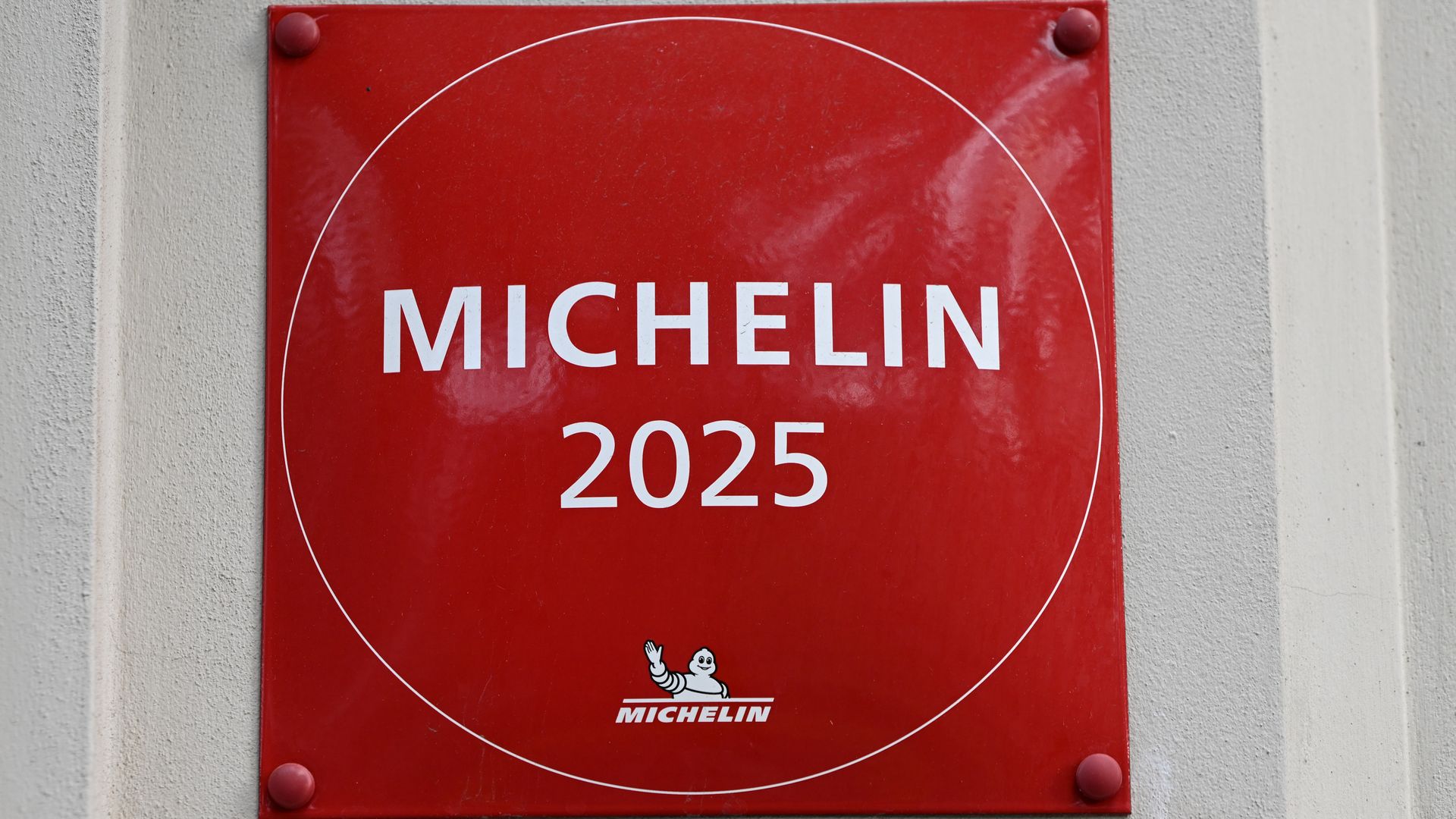 Red square plaque with white text reading "MICHELIN 2025" and the Michelin Man logo at the bottom, mounted on a beige textured wall.