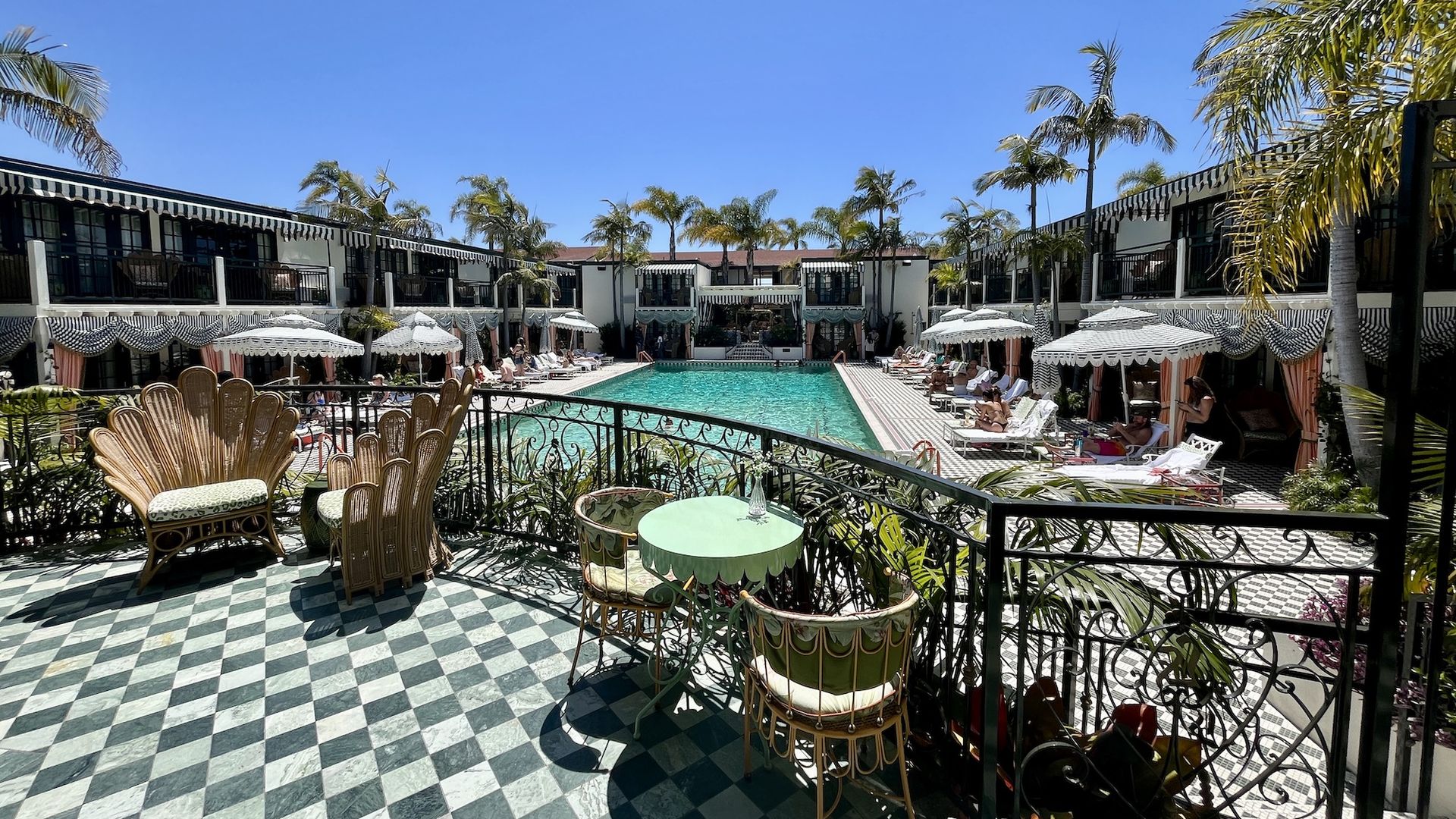 A view from a balcony overlooking a retro-style pool with cabanas.