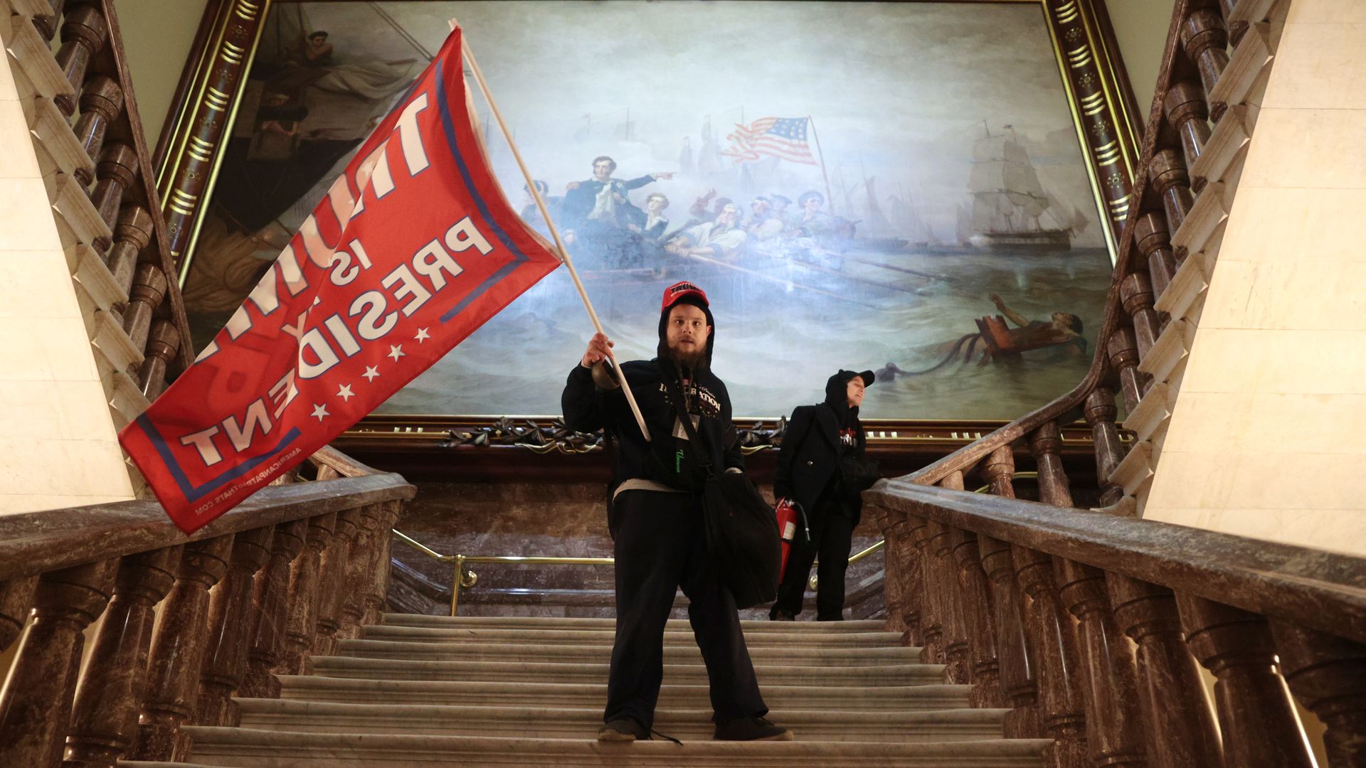 a protestor with a flag climbing steps inside the capitol