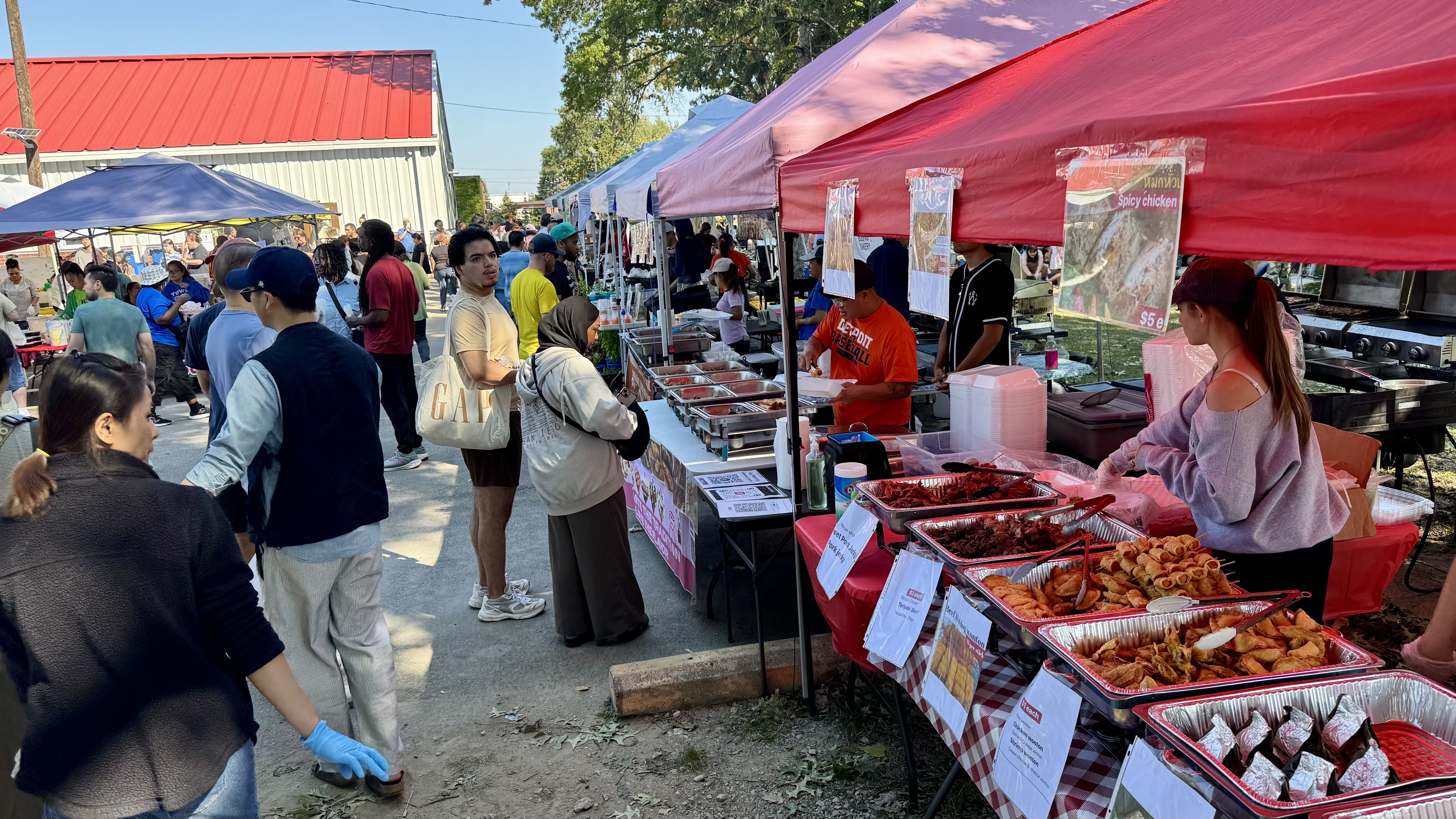 A view of the market, including trays of Thai food being sold by vendors in tents, and many attendees crowding around