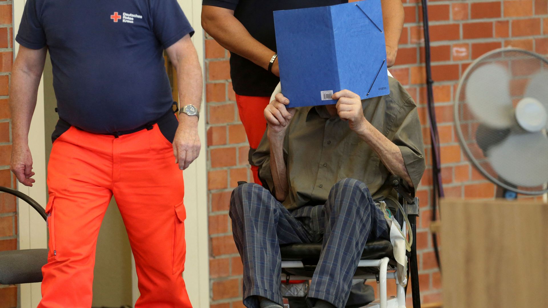 Former Nazi concentration camp guard Josef Schuetz (R) hides his face with a folder as he arrives on June 28, 2022 at a gym used as a makeshift courtroom in Brandenburg an der Havel, eastern Germany.