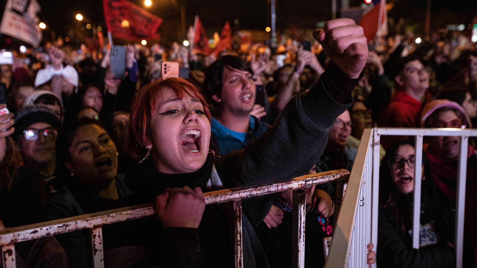 a young woman with red hair screams against a barrier, surrounding by other demonstrators in Chile on the 50-year mark of the coup that led to the dictatorship of Augusto Pinochet