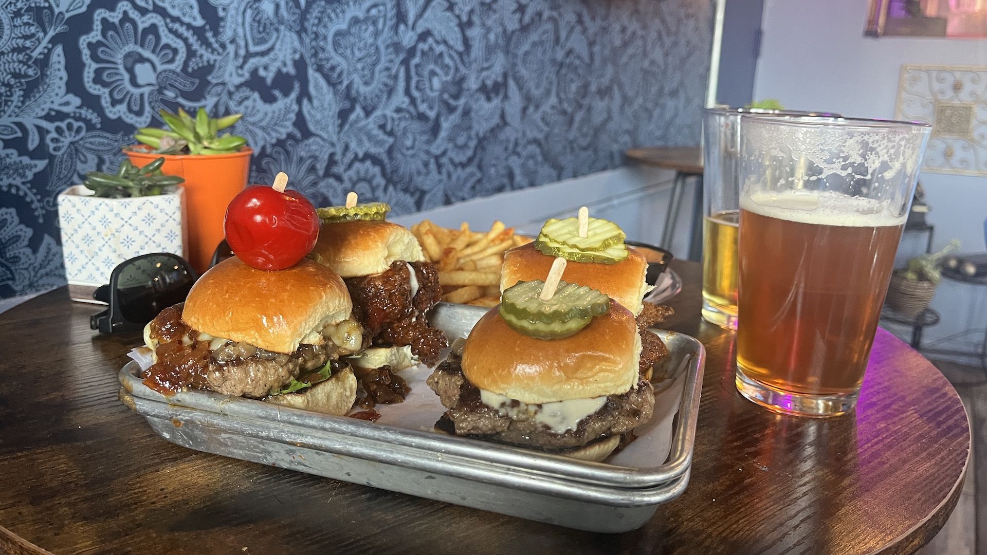 Four burger sliders on a tray with a beer.