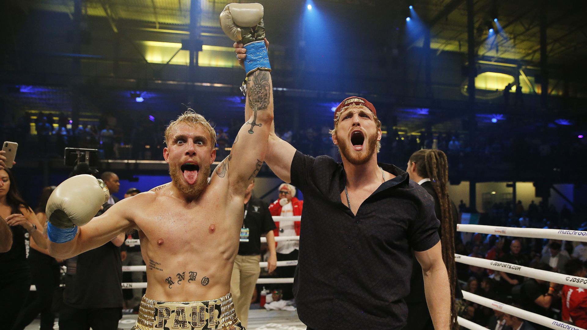 Logan Paul raises his brother Jake's hand in victory after a boxing match. 