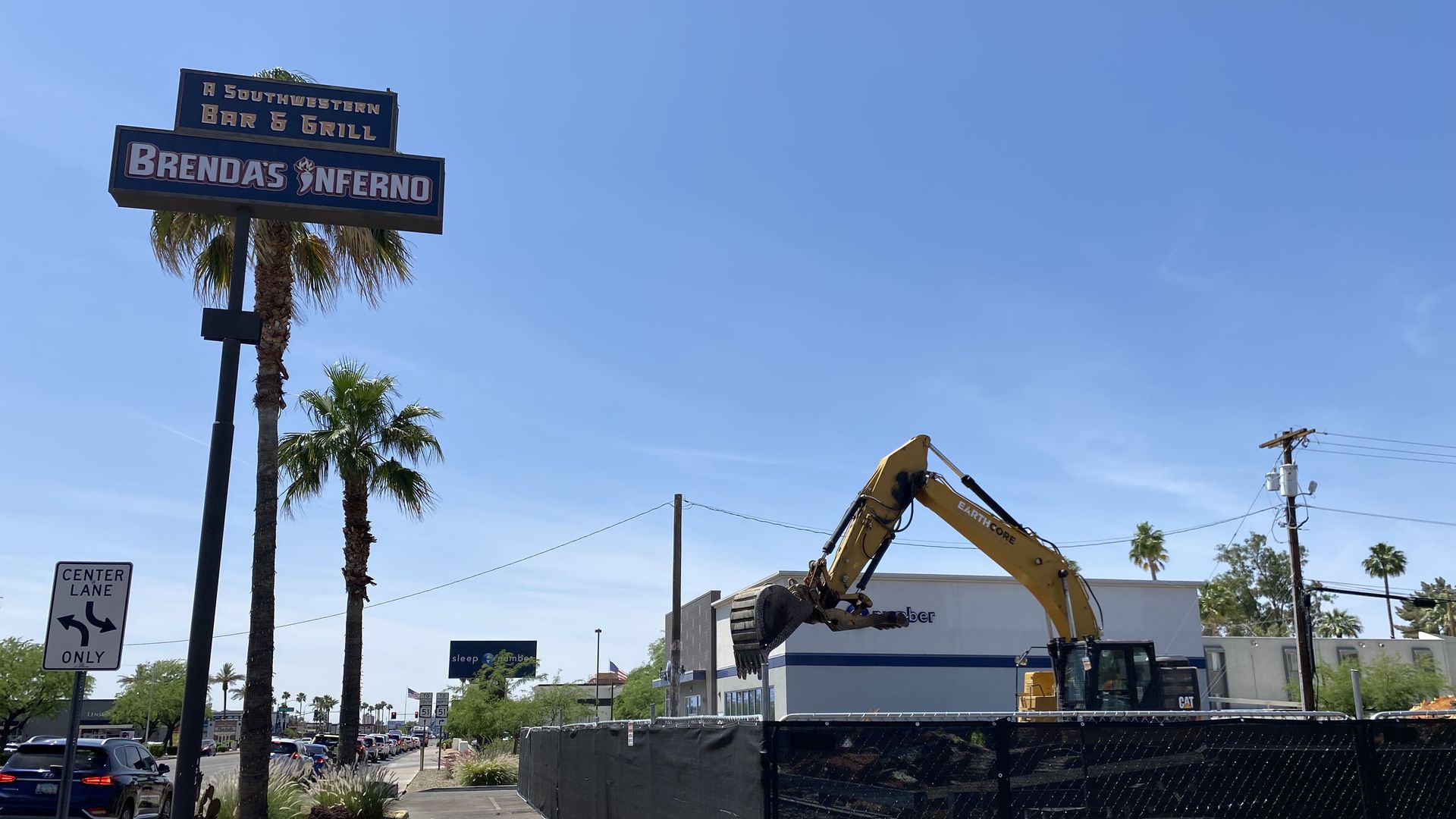 An excavator sorts through rubble in a fenced off site next to a sign that says Brenda's Inferno.