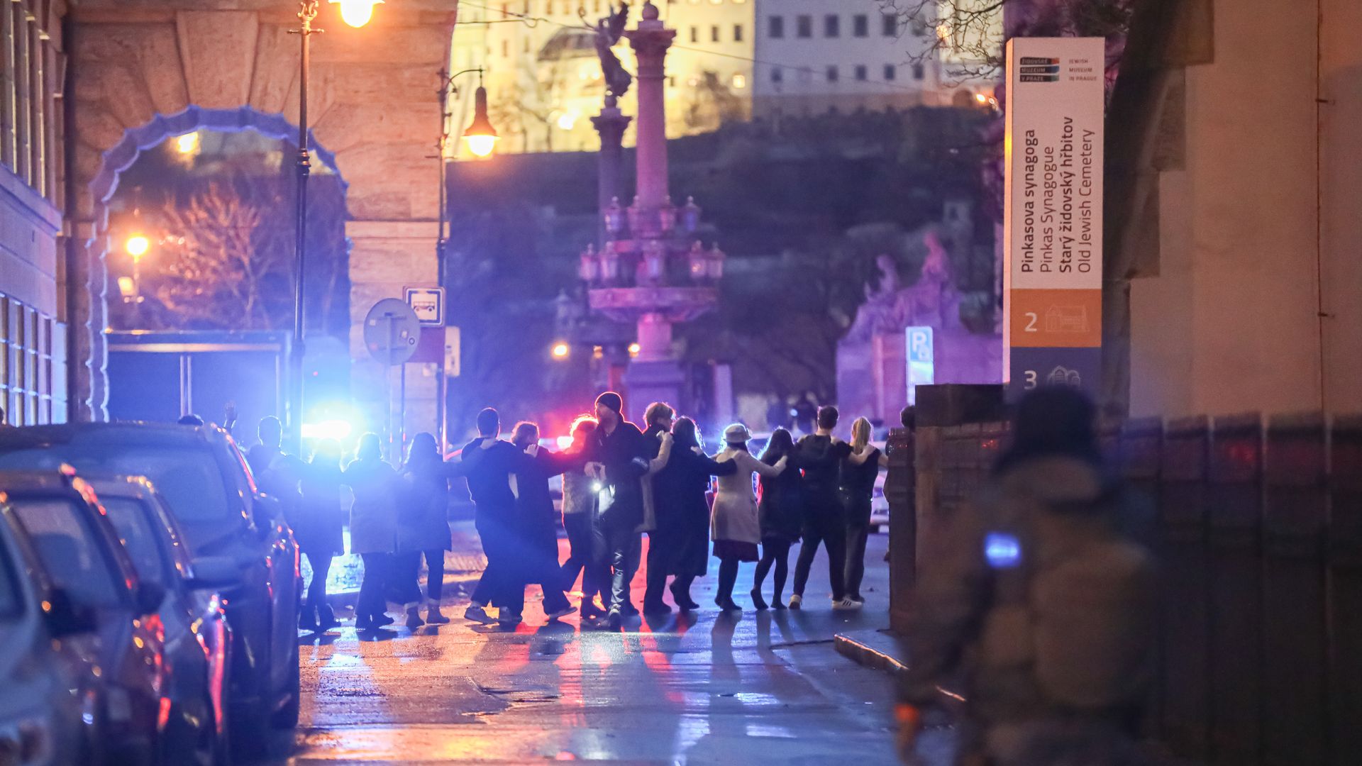 People in a huddle with police lights in the background in Prague