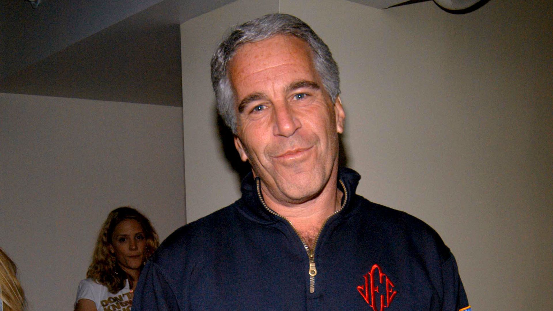 In this image, Epstein stands and looks at the camera while wearing a sweater pullover