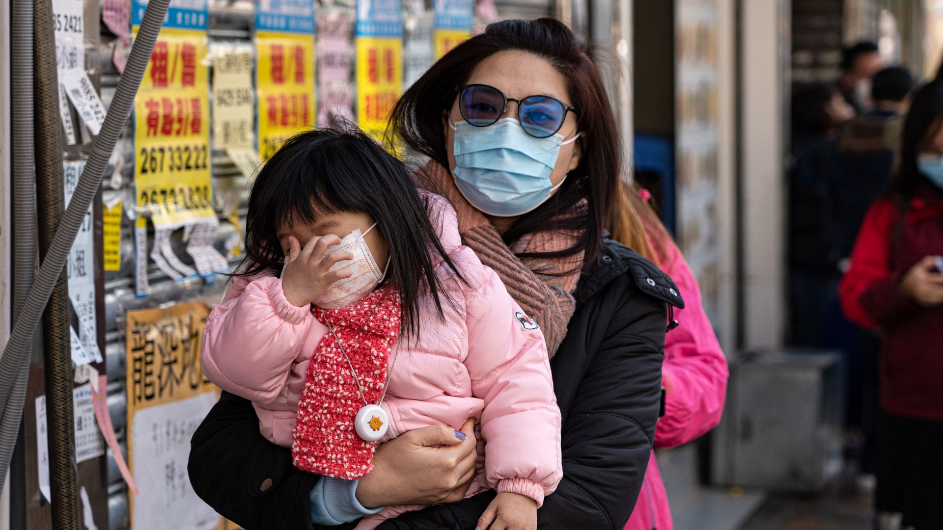 In this image, a mother holds her child as they both wear face masks in Hong Kong
