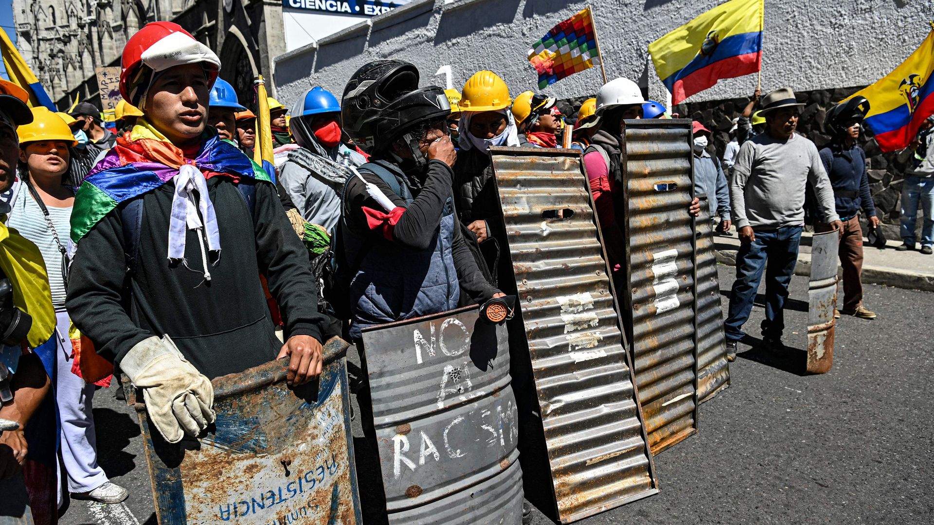 A group of protesters wearing helmets, capes and holding sheets of metal as protection walk through an anti-government protest in Ecuador