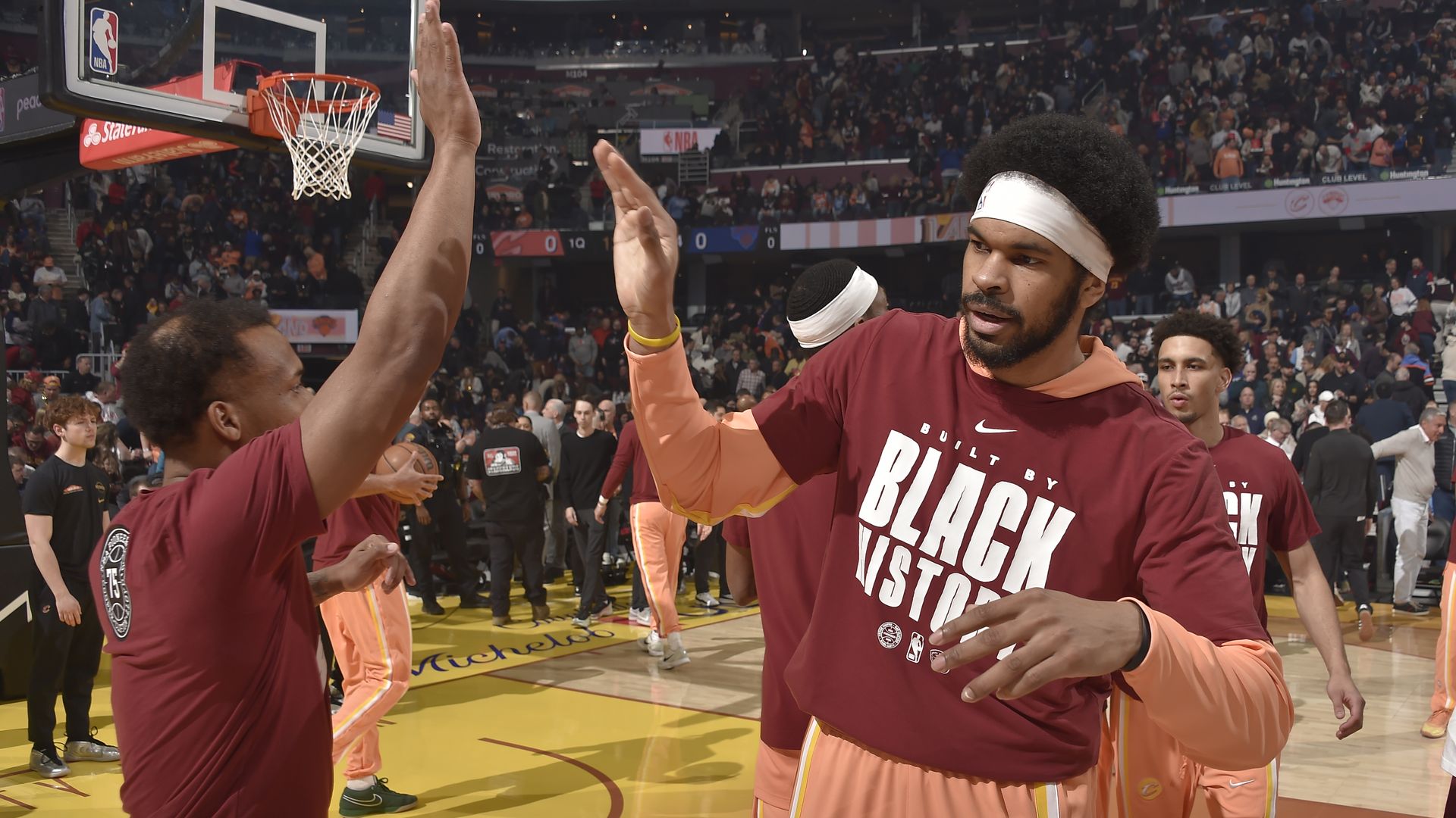 NBA basketball player in white headband and afro wearing red shirt with white "Black History" letters, high-fiving someone