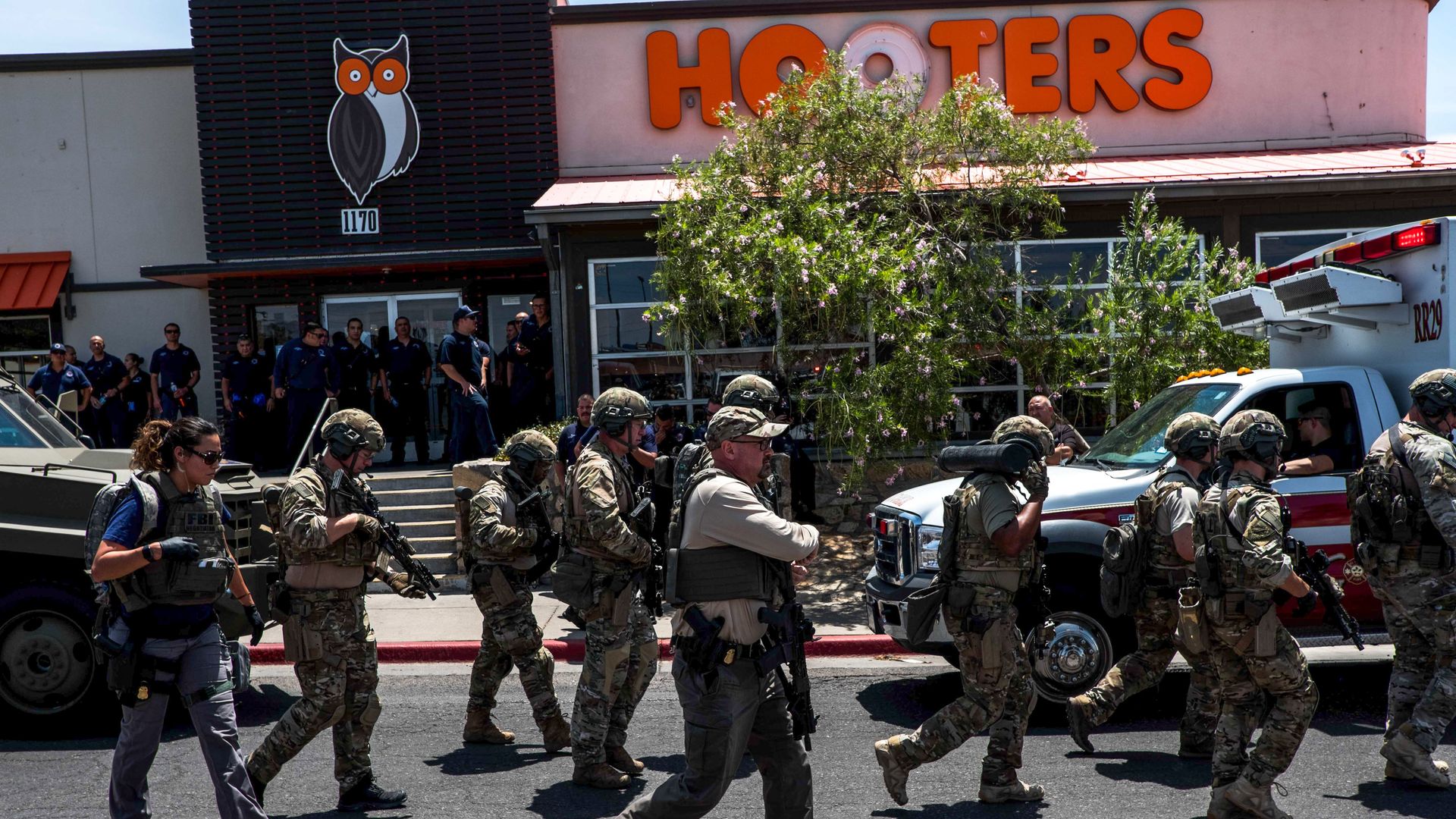 In this image, armed and fatigued officers hold rifles while walking past a Hooter's.