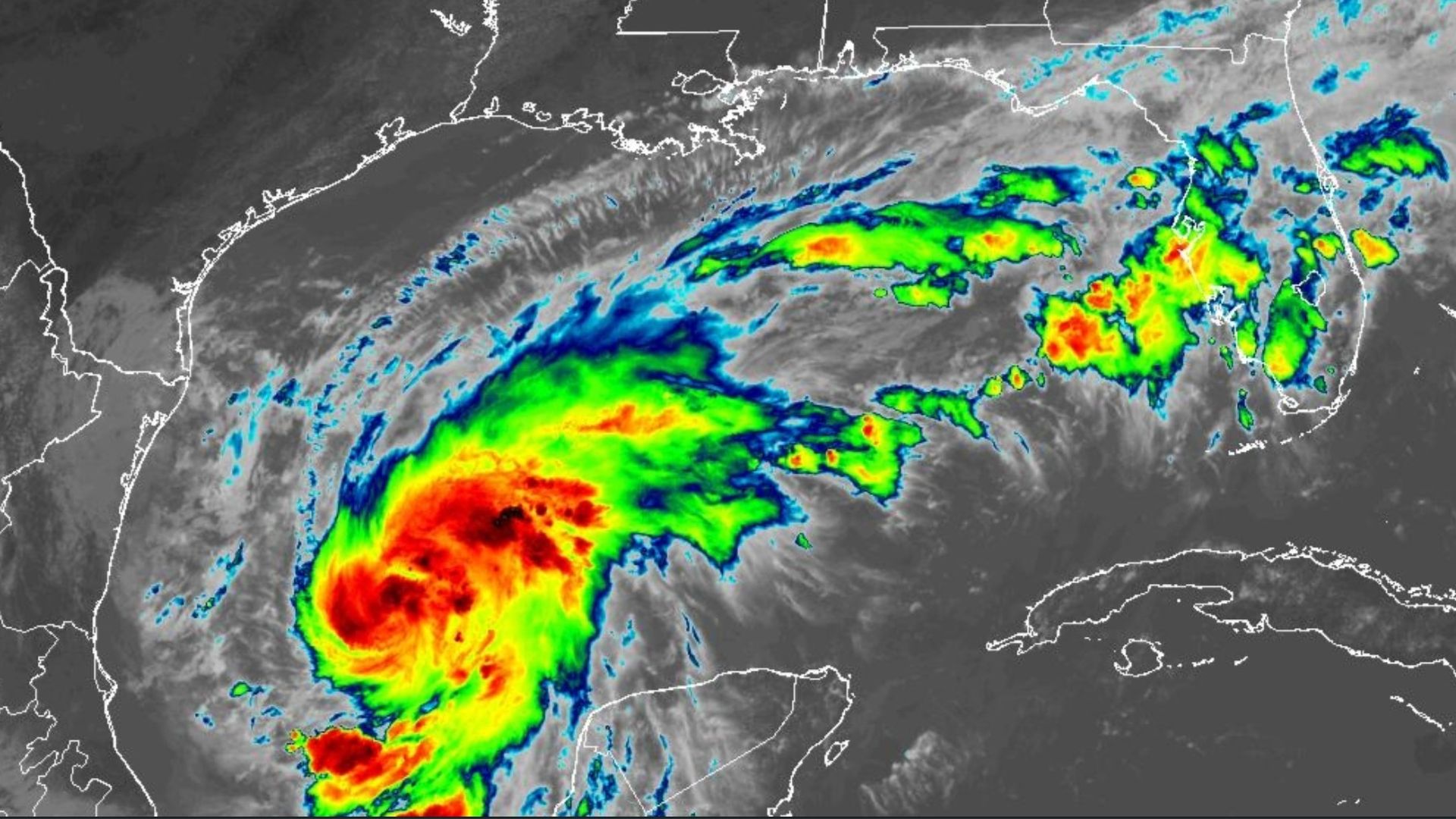 Infrared satellite image of a large tropical cyclone in the Gulf, with a bright red/orange core and vivid green rainbands, extending toward Cuba and the Florida coast.