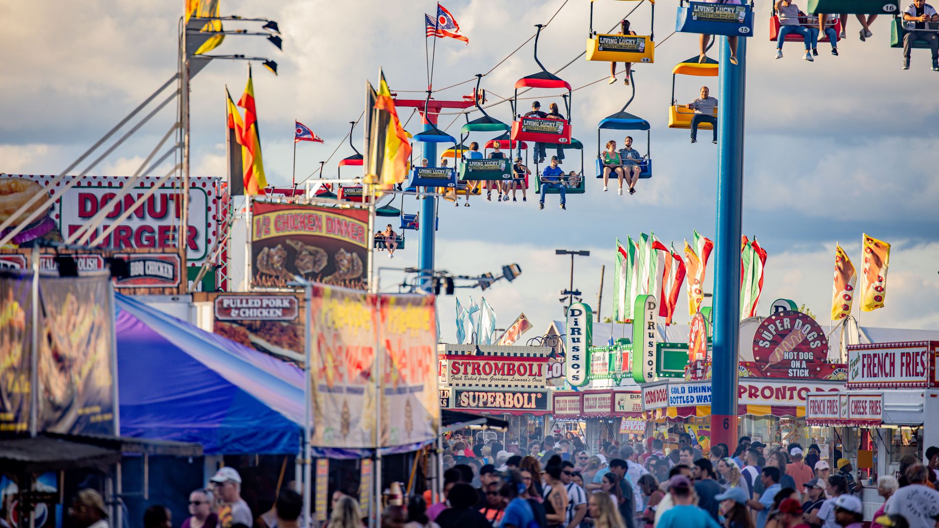 The midway of the Ohio State Fair, with food vendors, a skyride and people walking. 