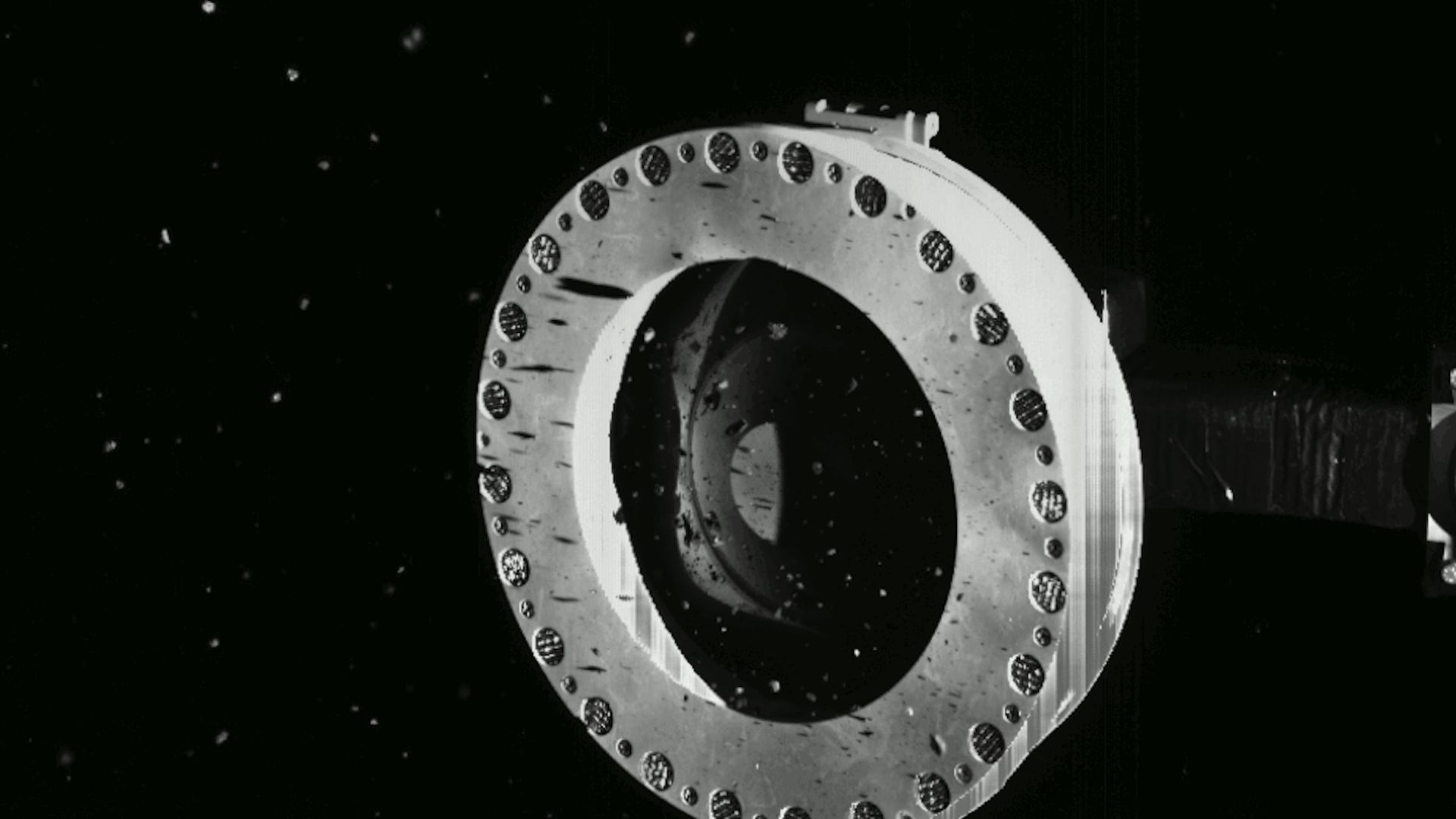 Particles of an asteroid sample floating around the sampling arm used to collect them in deep space