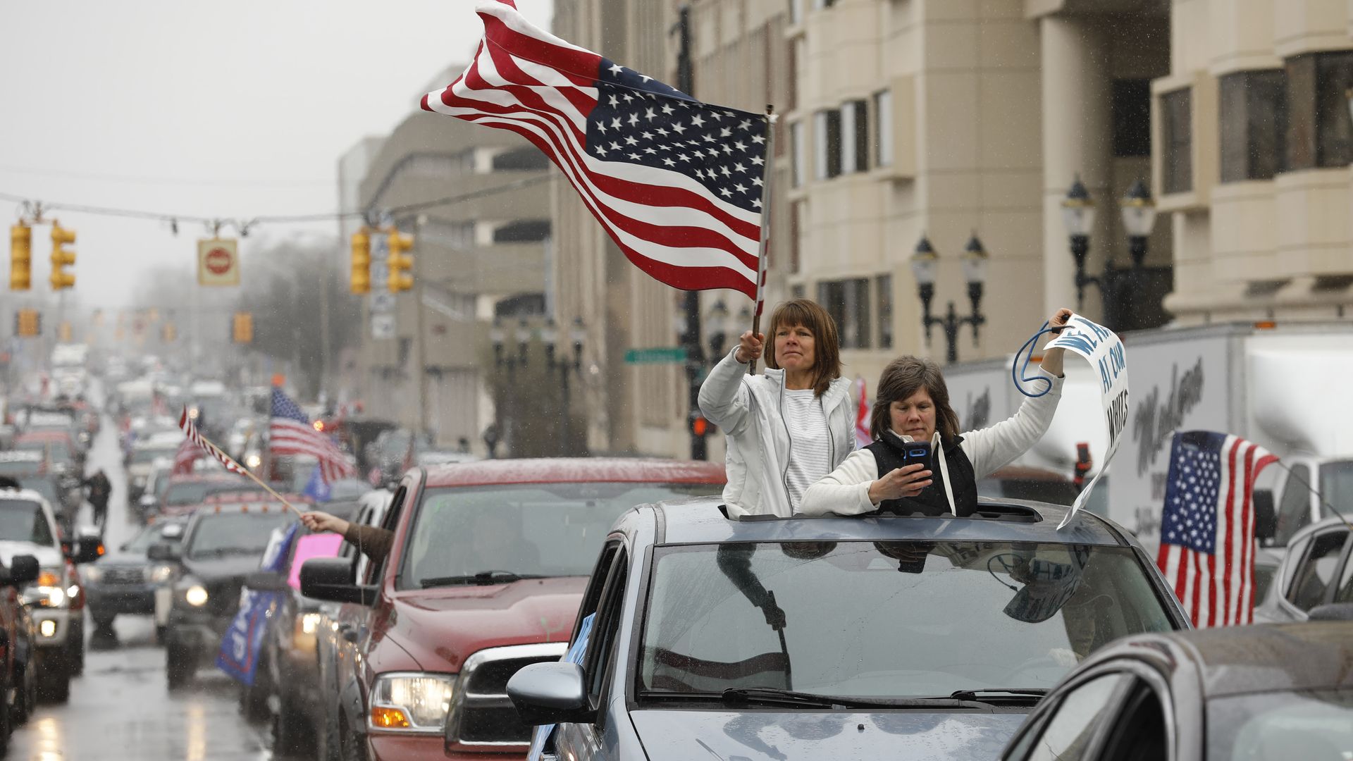 In this image, two women stand in the sunroof of an SUV