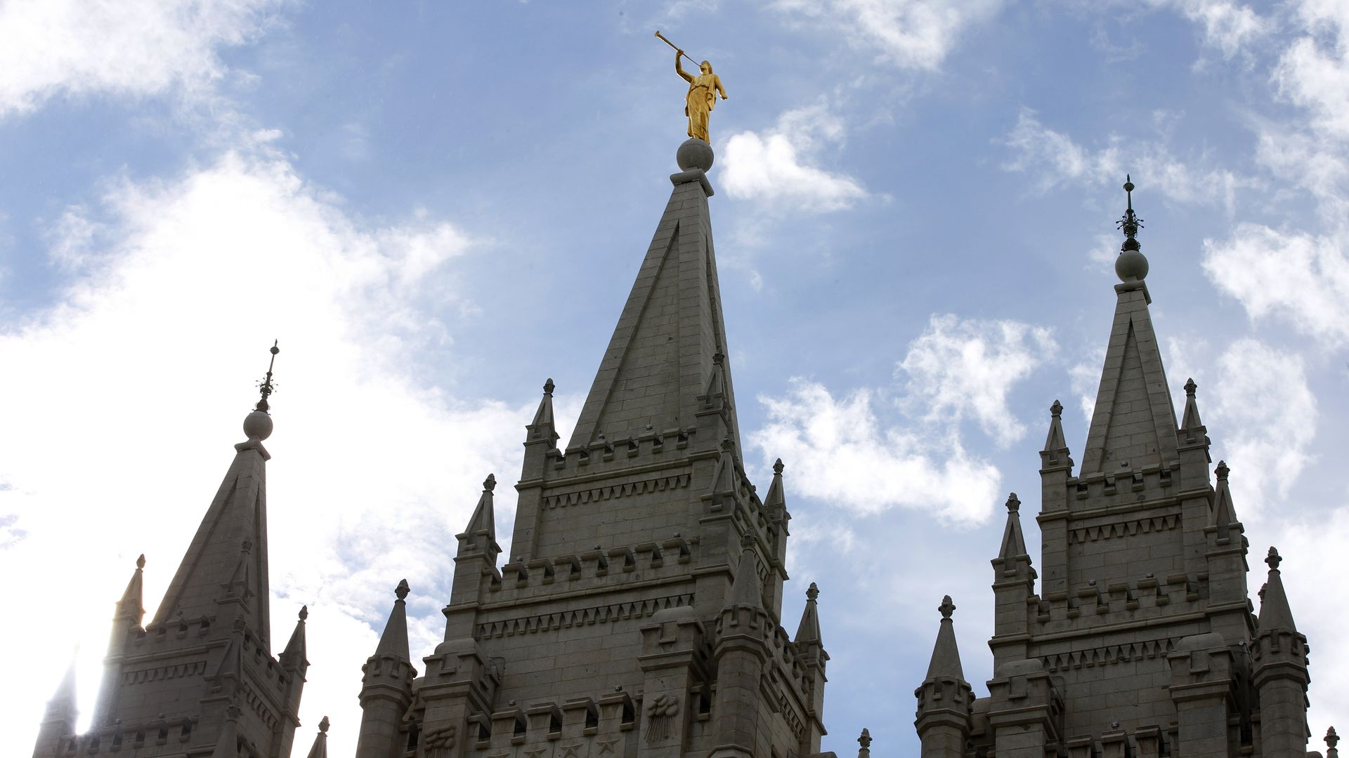 The steeples of the temple of the Church of Jesus Christ of Latter-day Saints are backed by a blue sky with clouds.