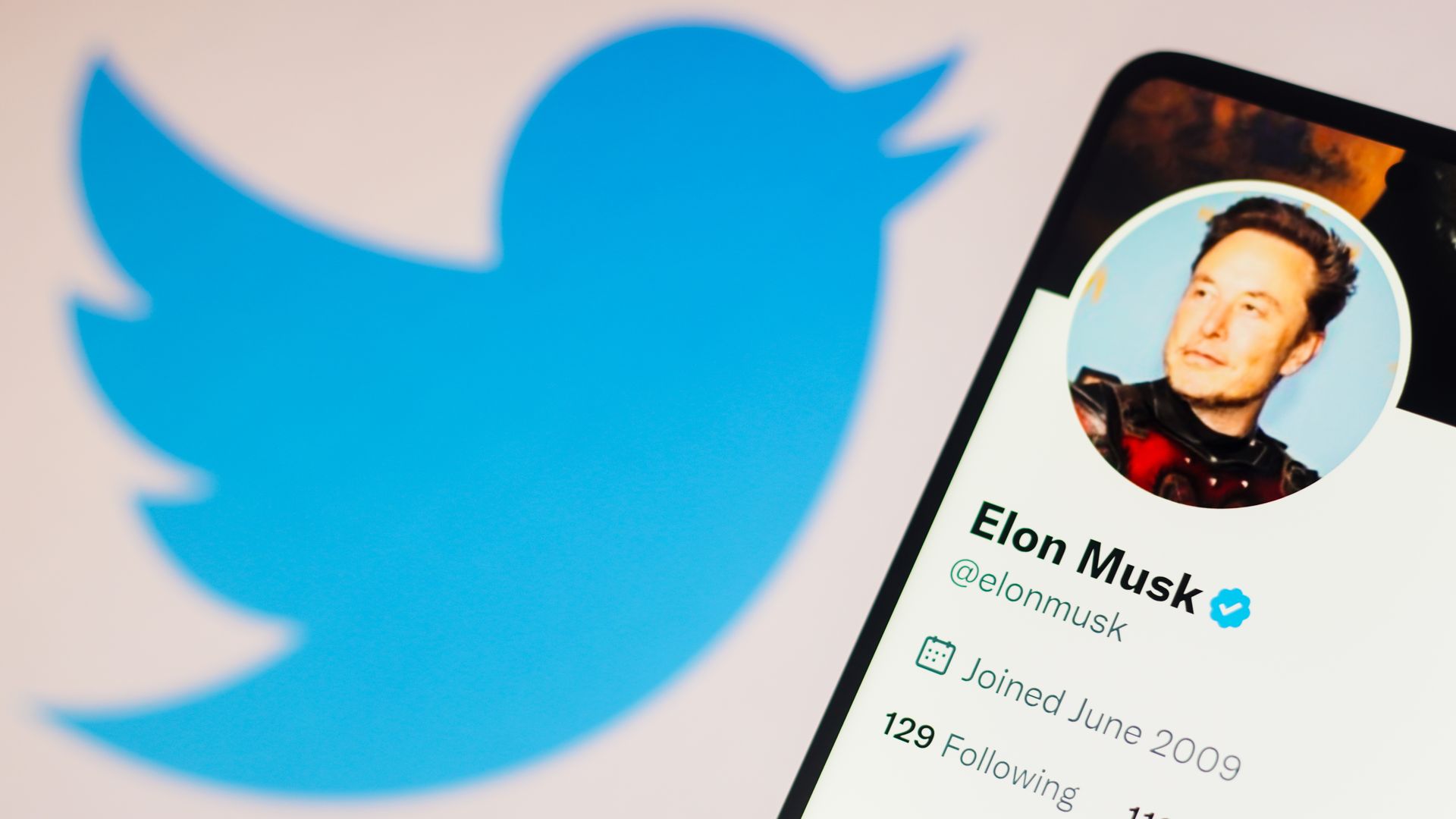 the Elon Musk Twitter account seen displayed on a smartphone and Twitter logo in the background. 
