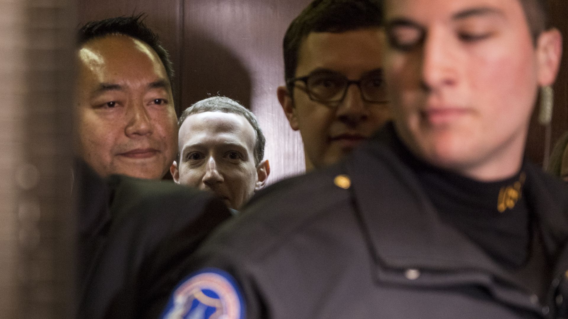 Mark Zuckerberg's face is half visible amid a group of other people