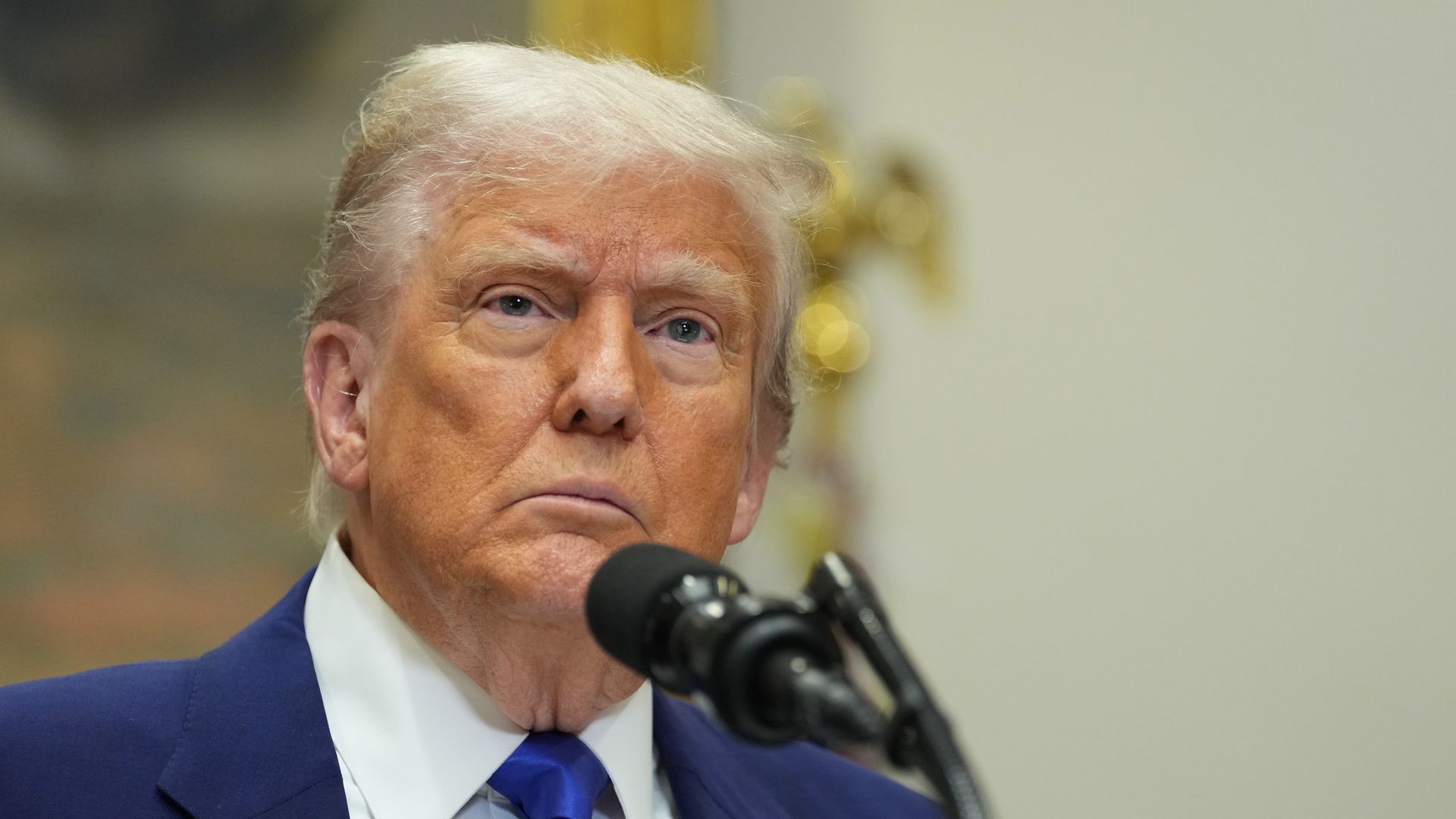 President Trump wearing a blue suit and speaking into a microphone.