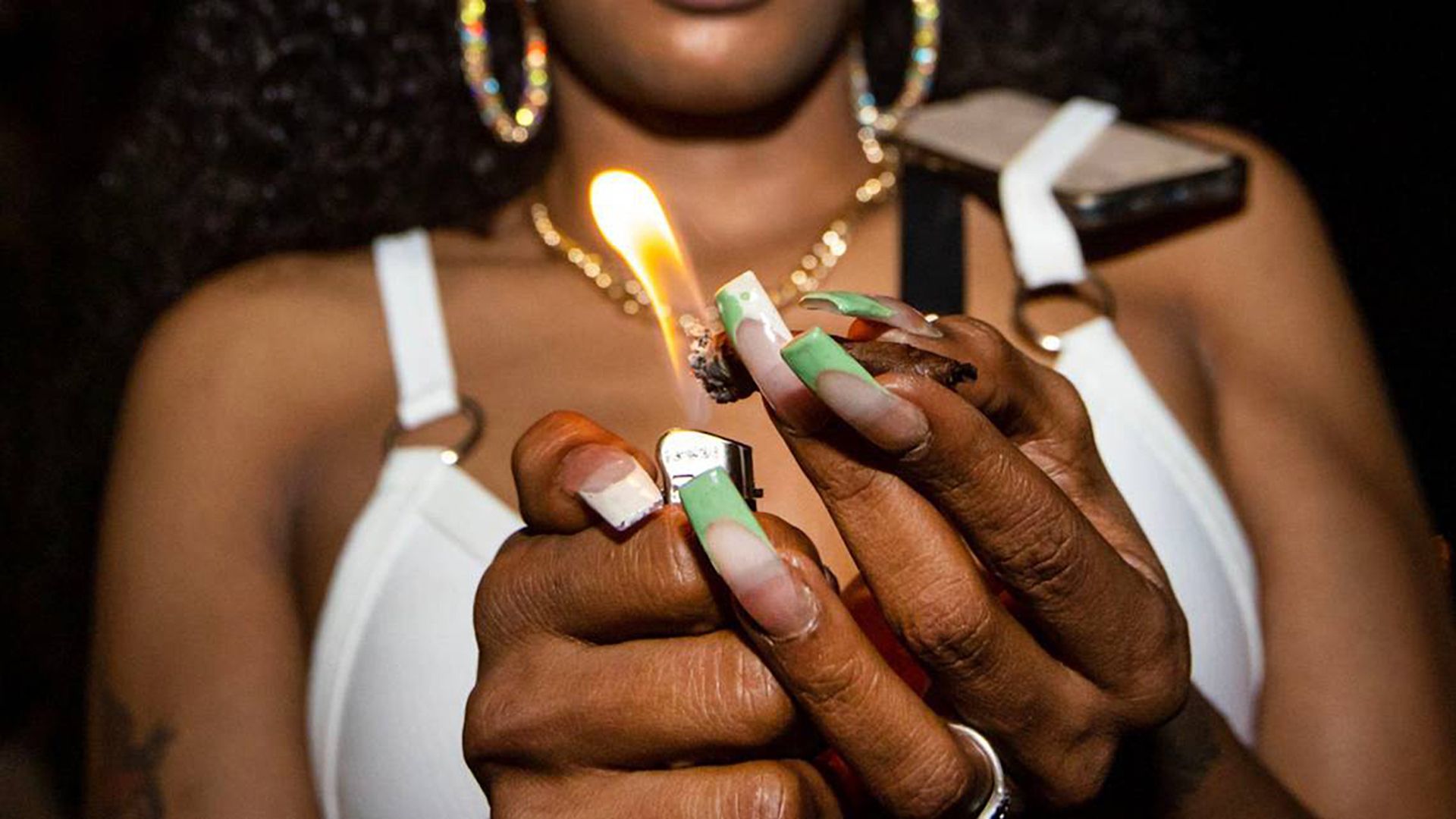 A woman with a green-tipped manicure holds a lighter to a blunt.
