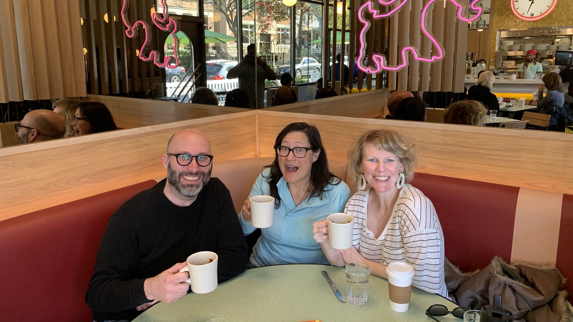 From left to right, Justin Kaufmann, Monica Eng and Carrie Shepherd smile while holding up coffees in a booth at Chicago's Little Goat Diner.