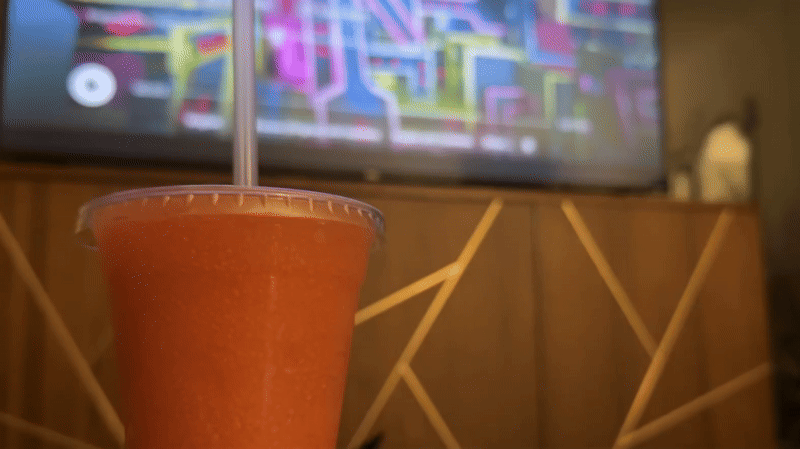 A gif of a black cat looking at a clear plastic cup with a frozen drink inside