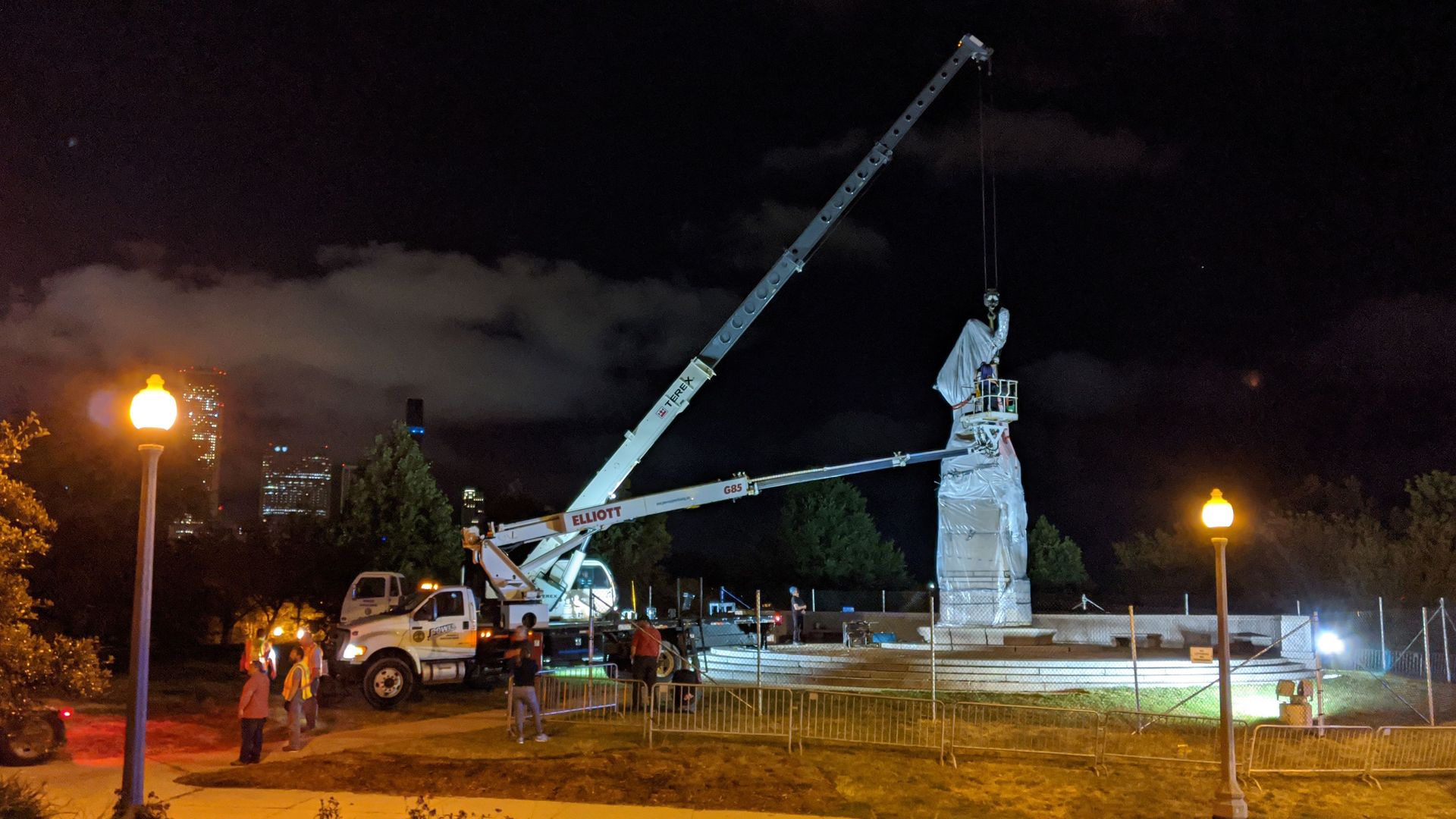 Photo of construction cranes removing a statue. 