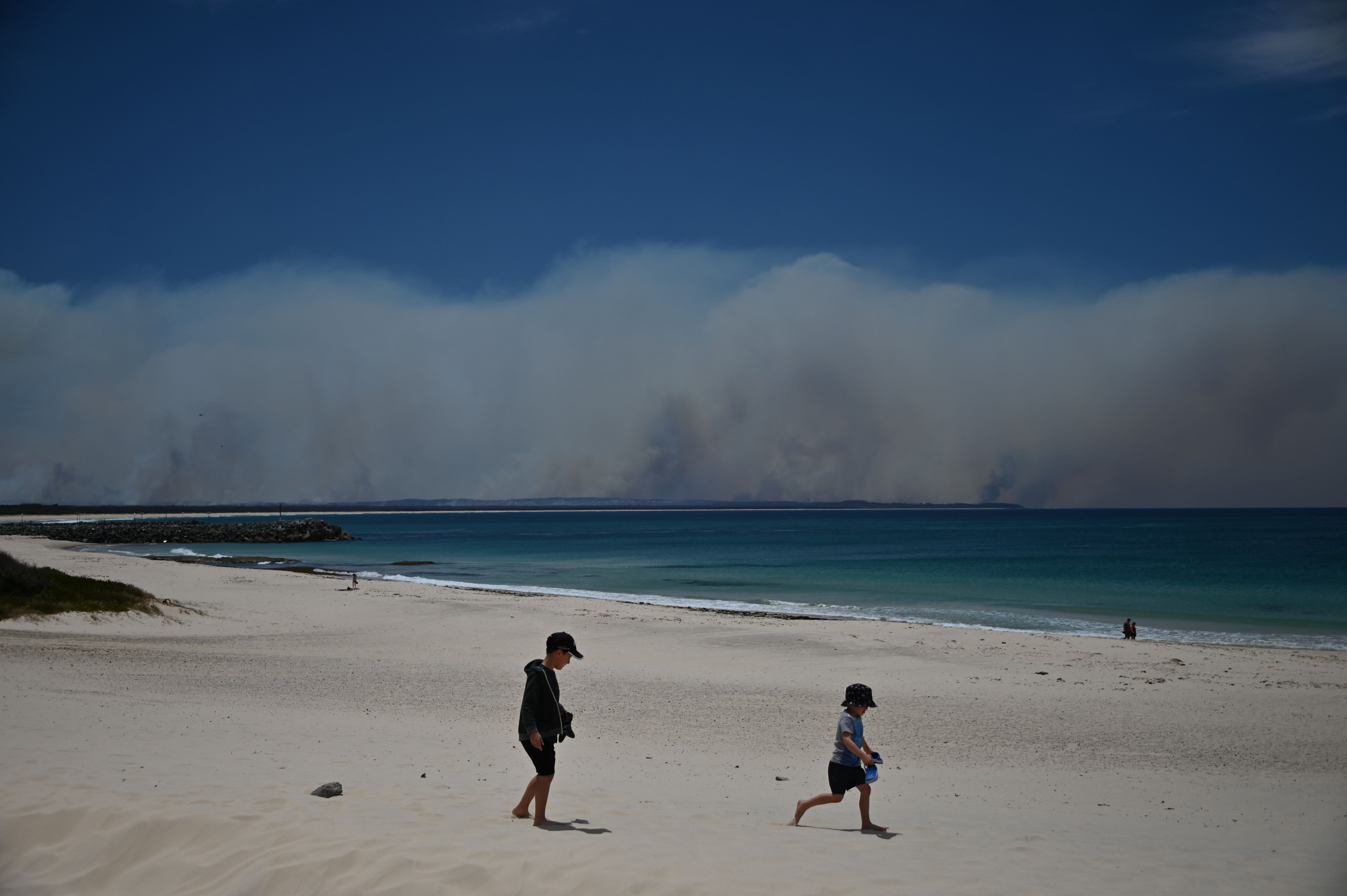 Bushfires burn in the distance as children play on a beach in Forster, 300km north of Sydney on November 9