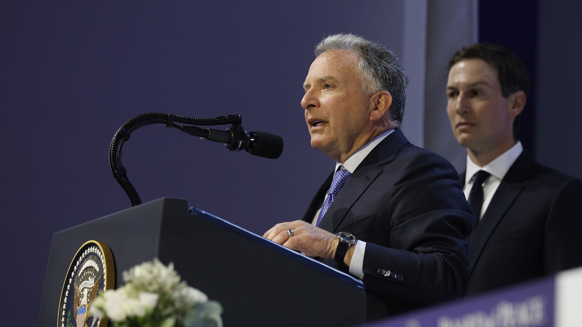 Steve Witkoff speaking at a podium, with Jared Kushner standing behind him.