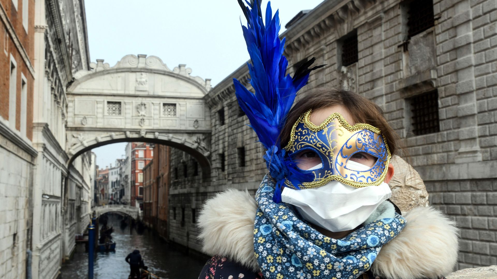 A young tourist wearing a protective facemask and a Carnival mask visits the streets of Venice