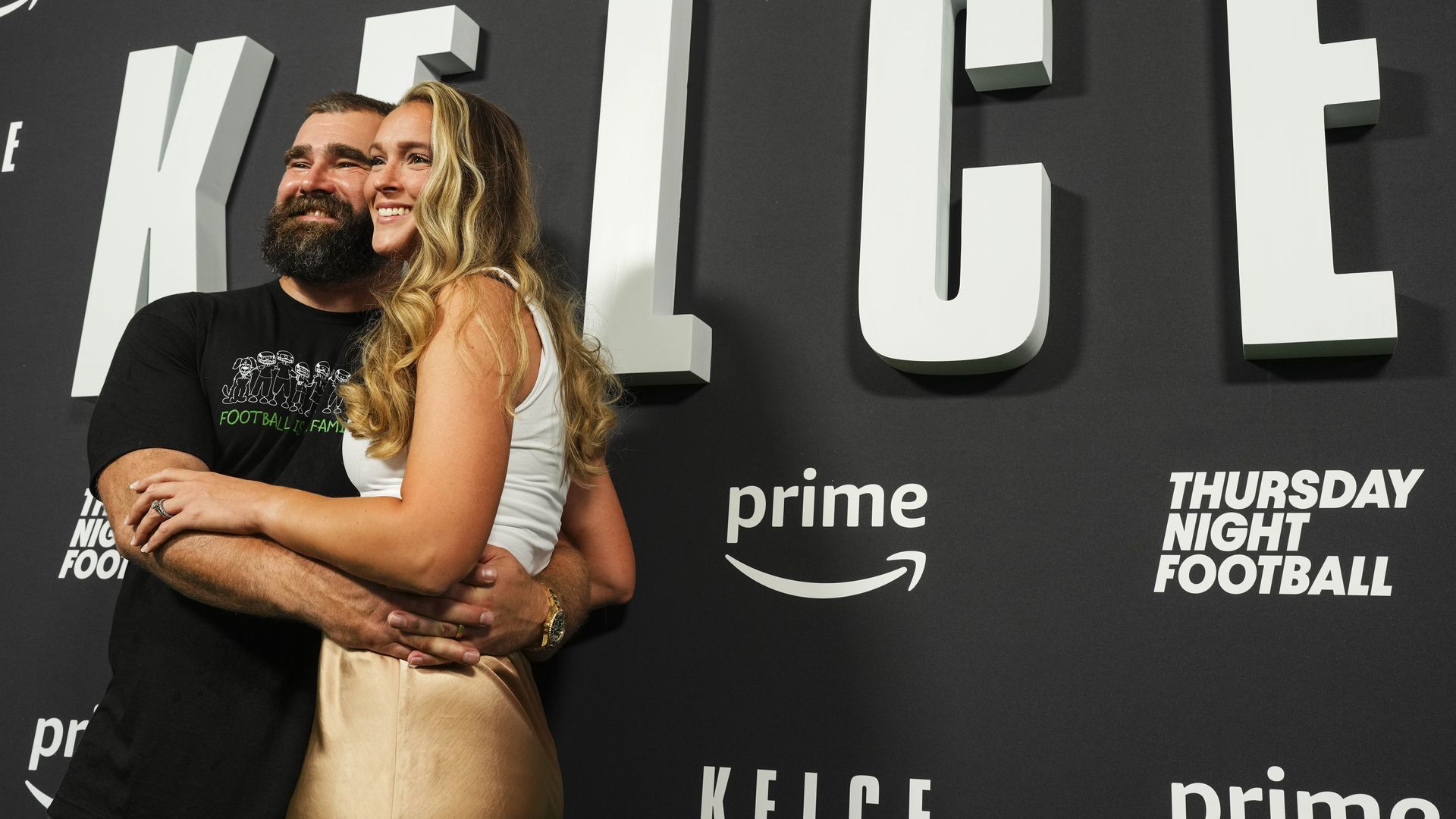 Kylie and Jason Kelce pose for a photo in front of a "Kelce" poster.