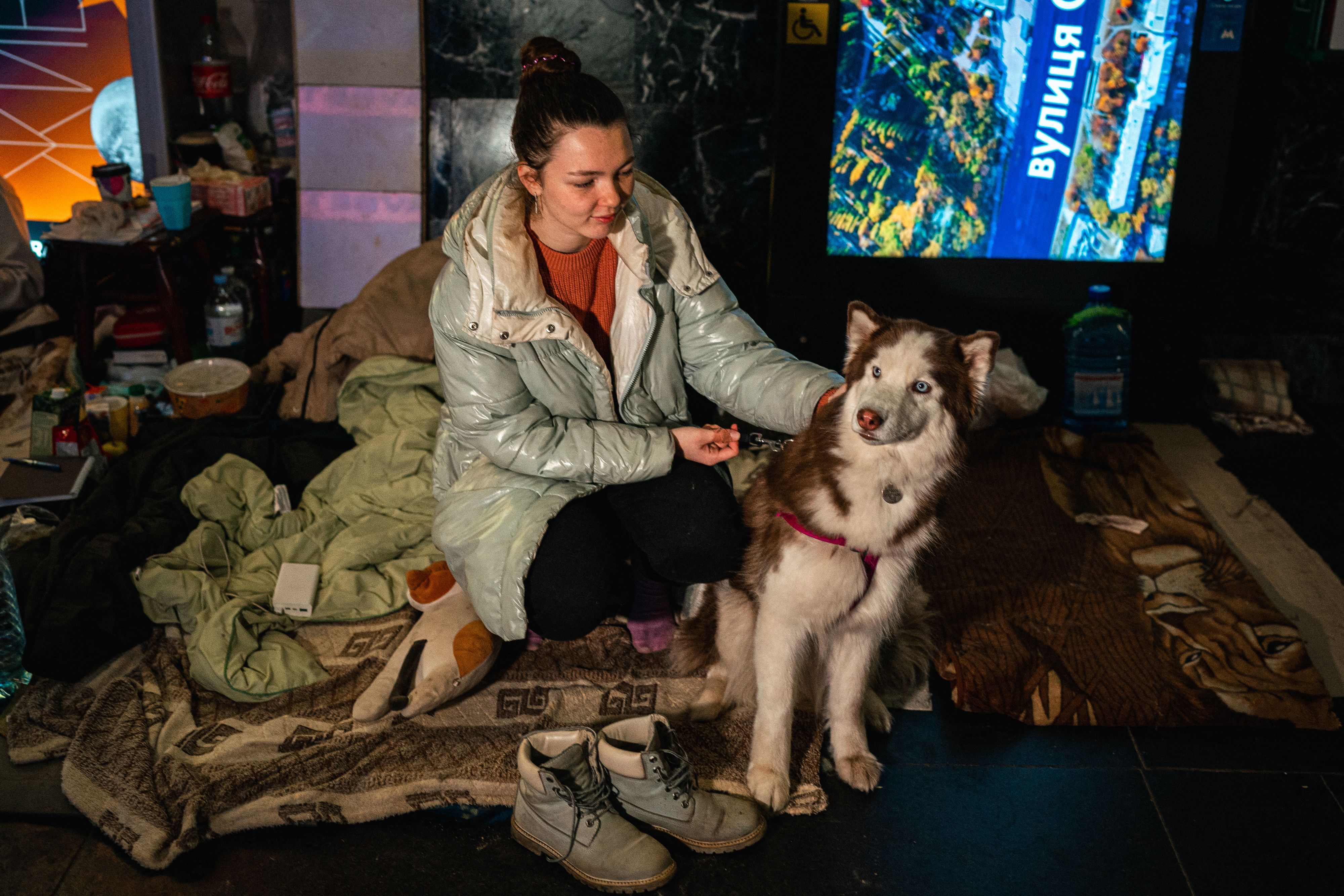 A woman and her dog sit on a makeshift bed in a underground metro station used as a bomb shelter in Kyiv on March 8