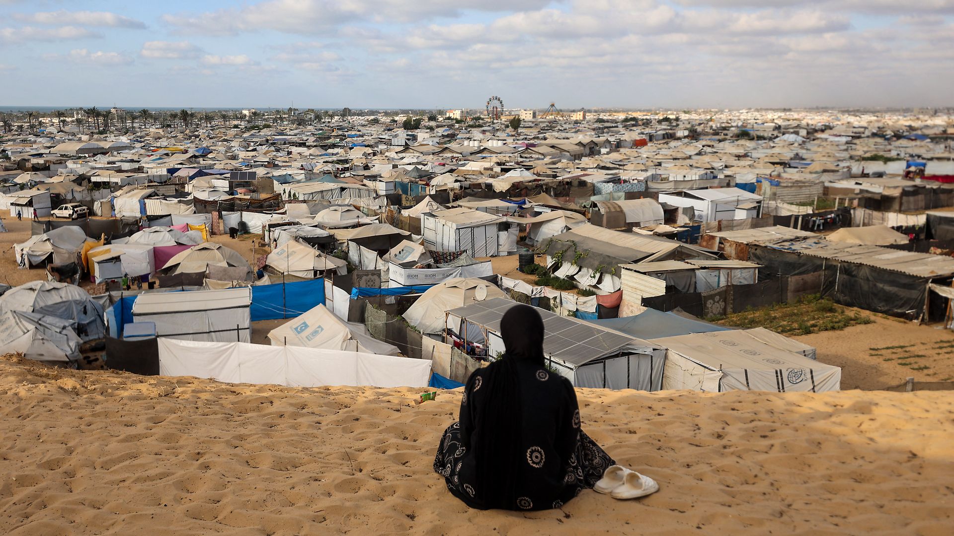 A woman dressed in black sits overlooking a camp in Gaza
