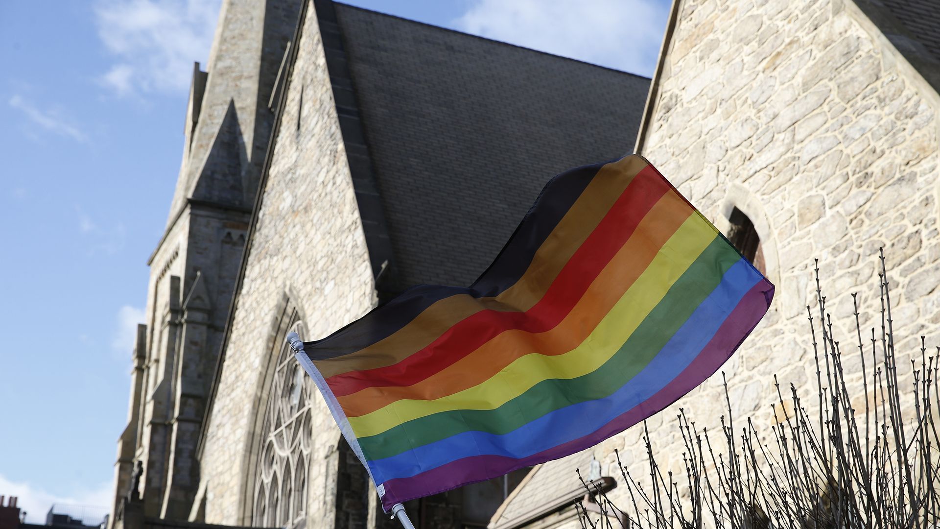 In this image, an LGBTQ pride flag waves in front of a church.