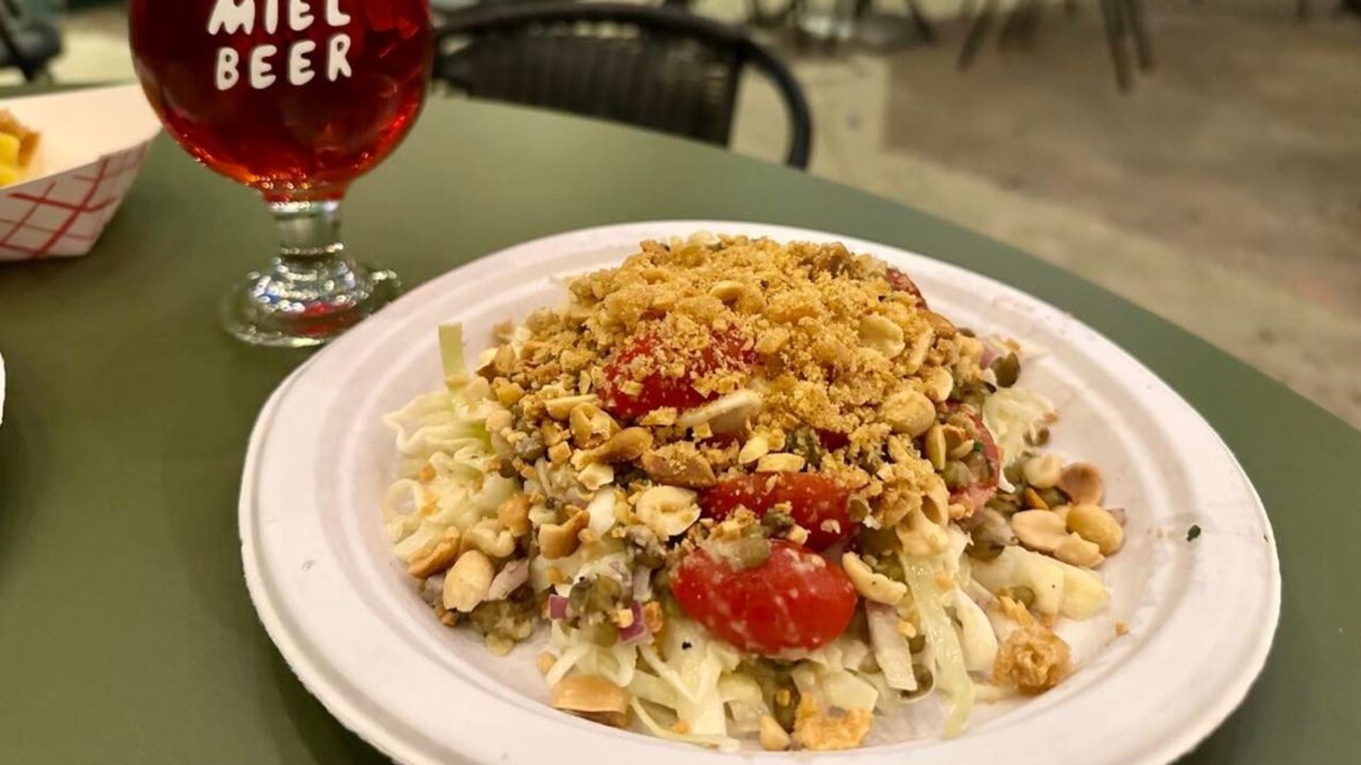 Photo shows a salad on a paper plate on a green table. 