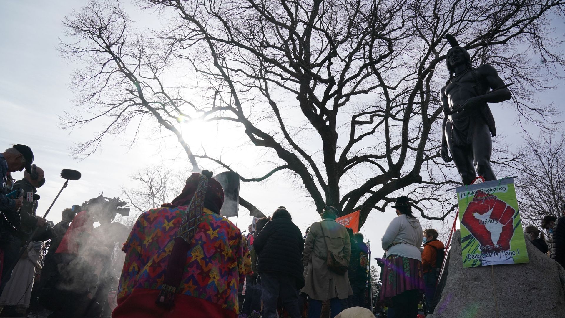 A statue of a man with a one-feather headdress above people with their heads bowed.
