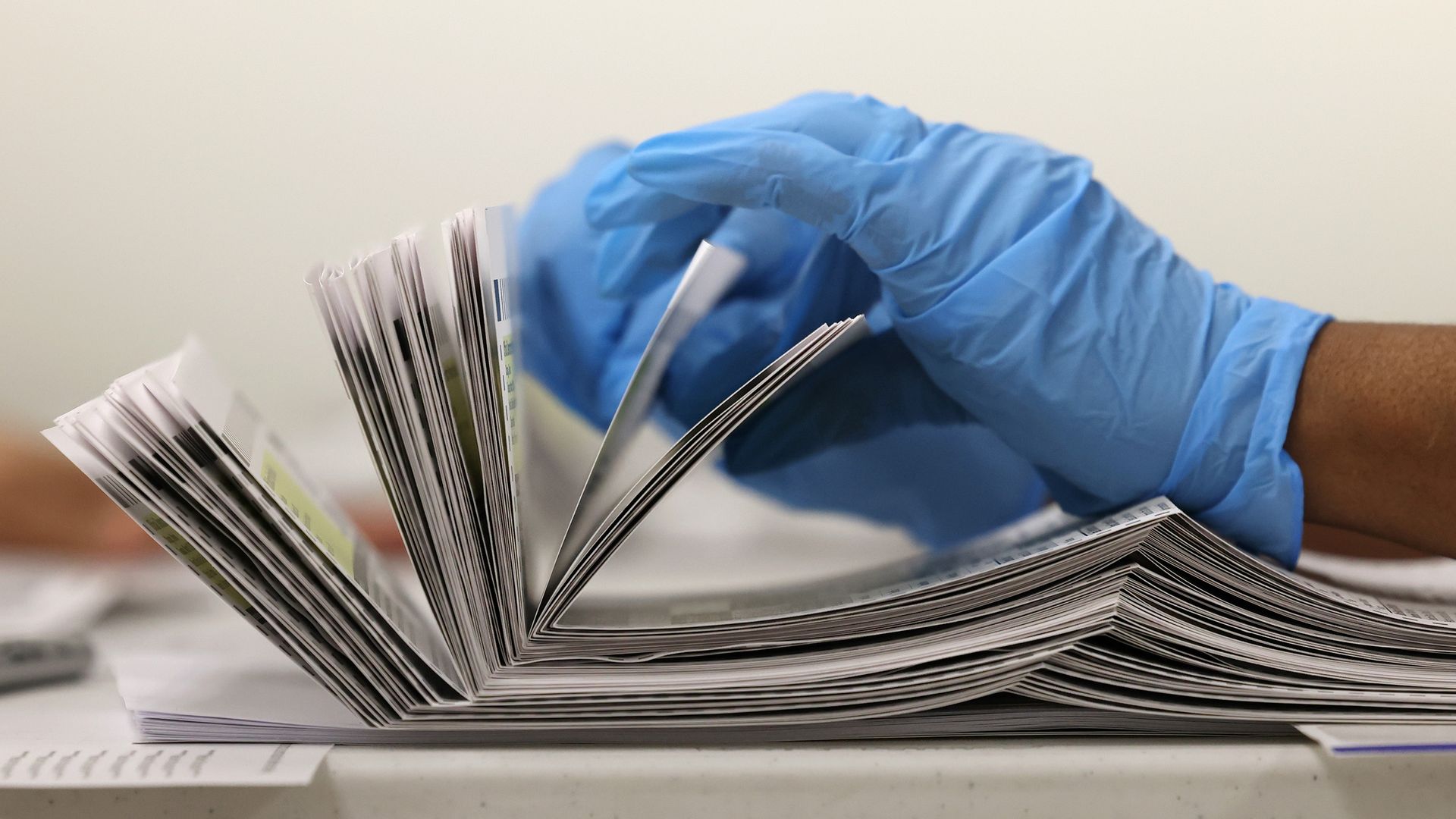 A pair of hands with gloves sorts through mail-in ballots 