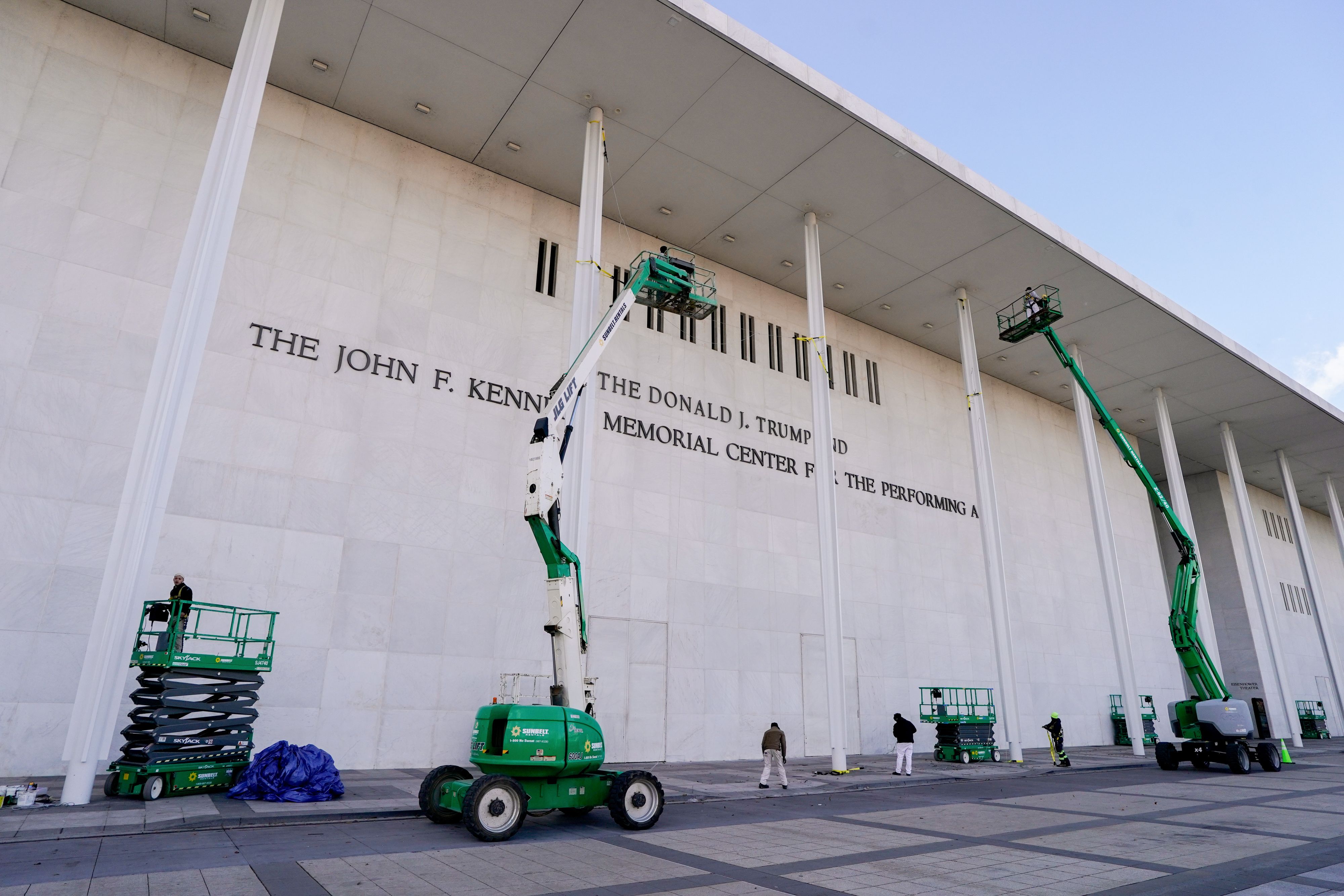 Workers affix signage adding US President Donald Trump's name on the facade of the Kennedy Center in Washington, DC, US, on Friday, Dec. 19, 2025. The board of the John F. Kennedy Center for the Performing Arts voted Thursday to rename Washington's premier arts venue after President Donald Trump as